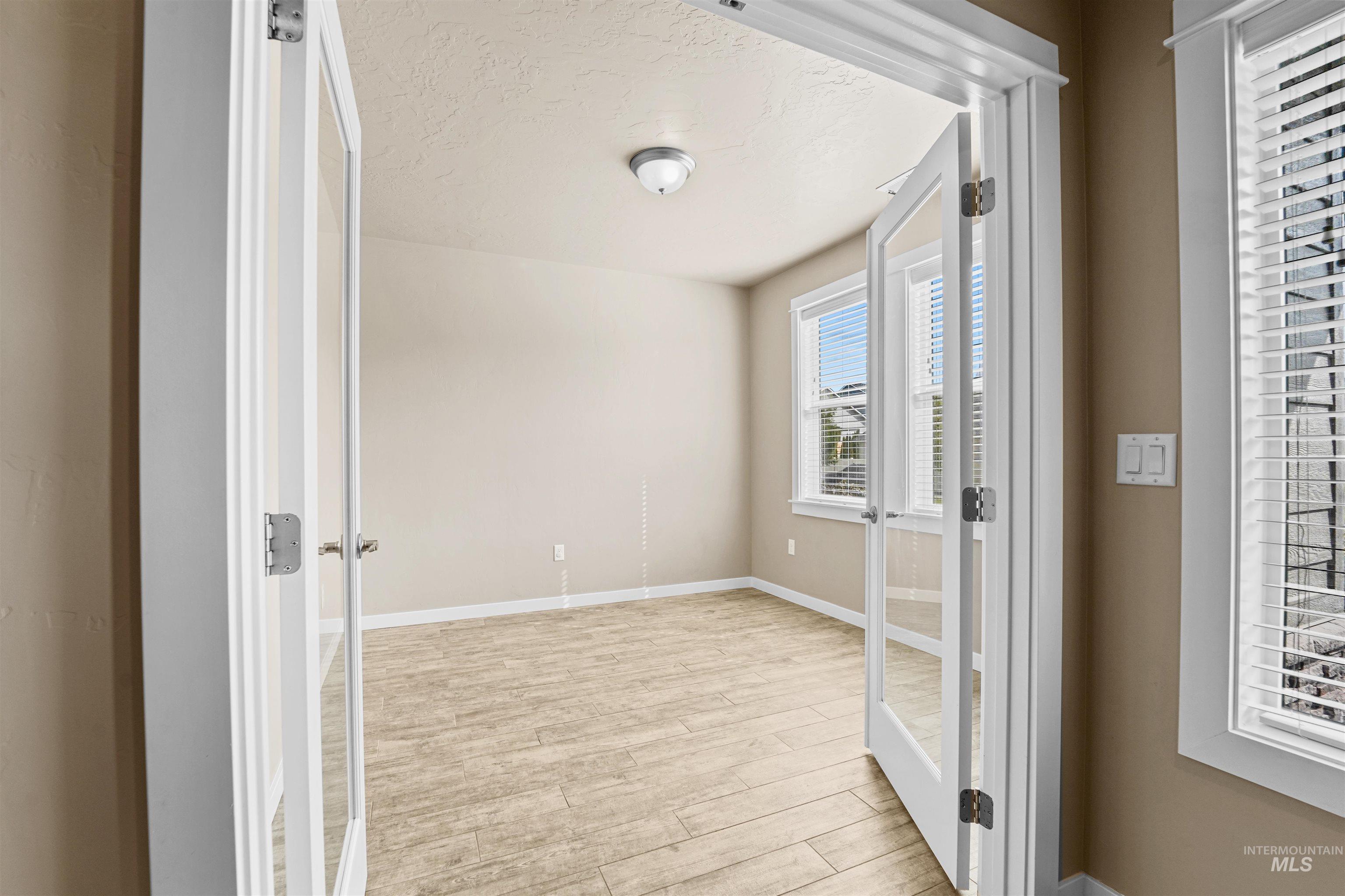 Spare room featuring french doors, light wood-type flooring, and a textured ceiling