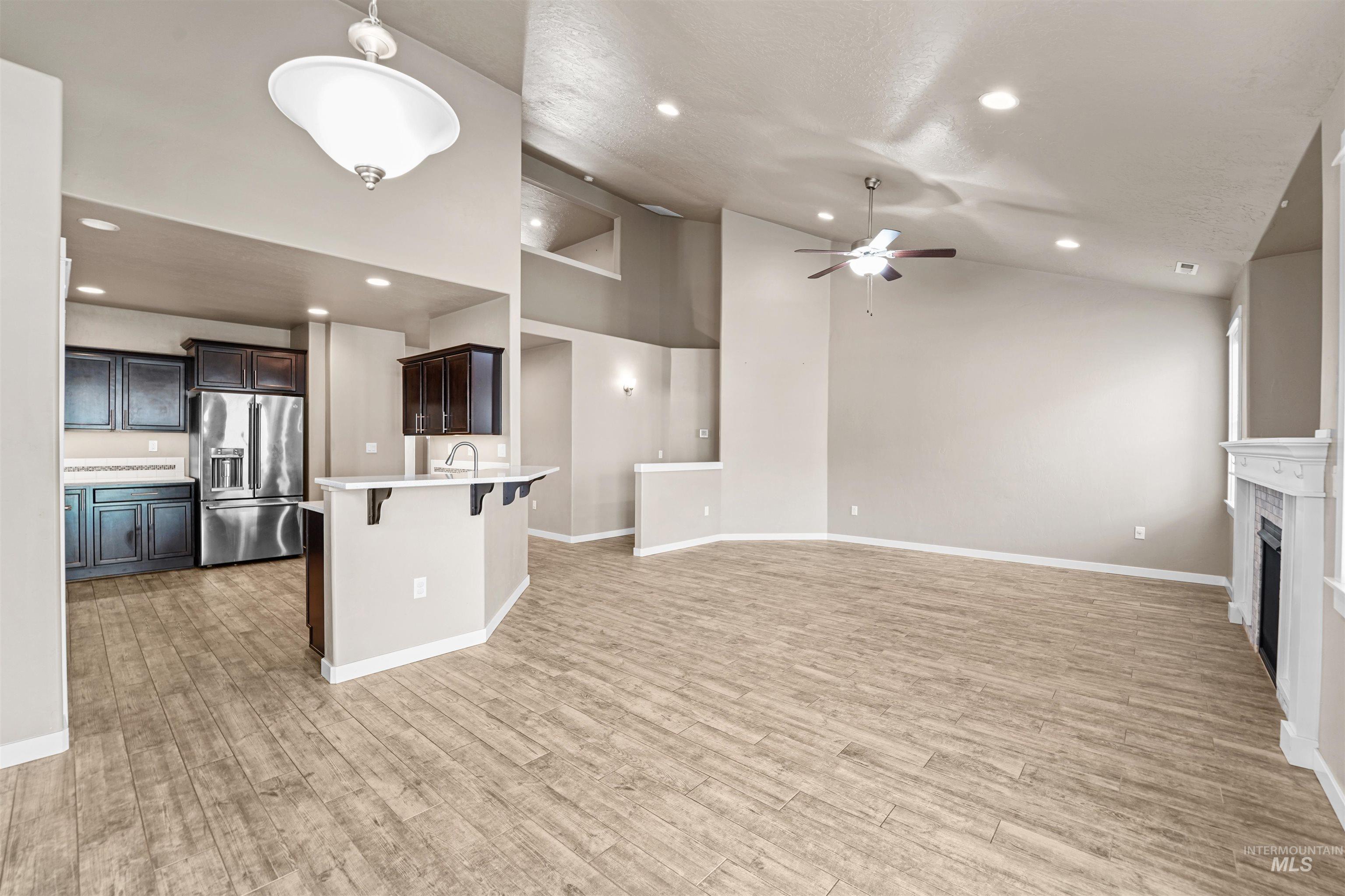 Unfurnished living room featuring a fireplace, recessed lighting, high vaulted ceiling, ceiling fan, and light wood-type flooring