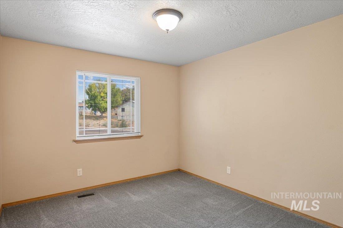 Carpeted empty room featuring a textured ceiling and baseboards