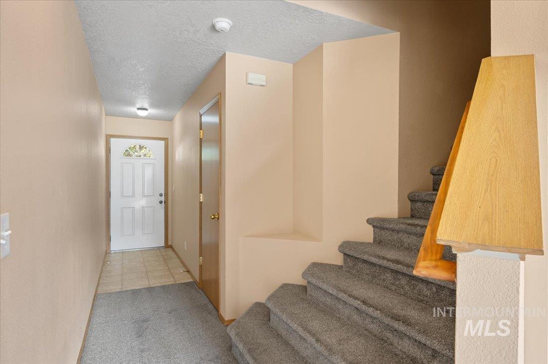 Staircase with a textured ceiling, carpet, and tile patterned floors