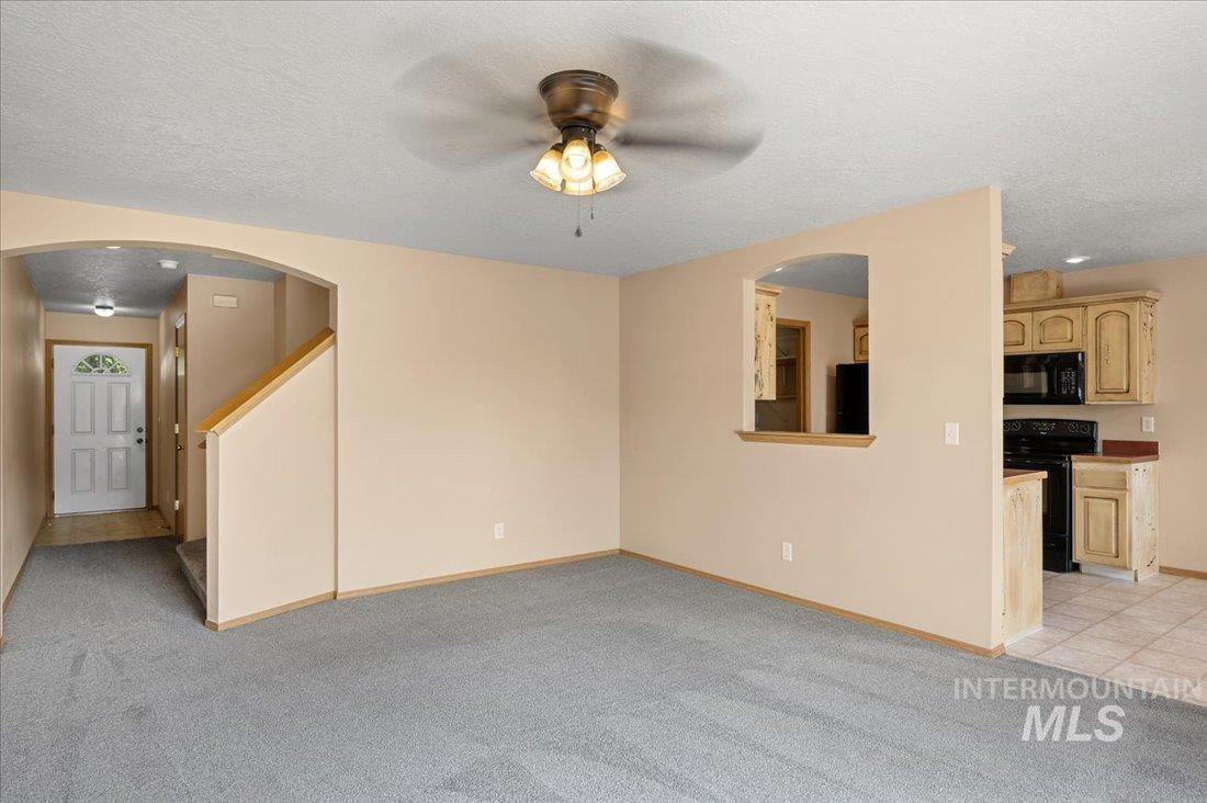 Unfurnished living room with a textured ceiling, light carpet, a ceiling fan, and arched walkways
