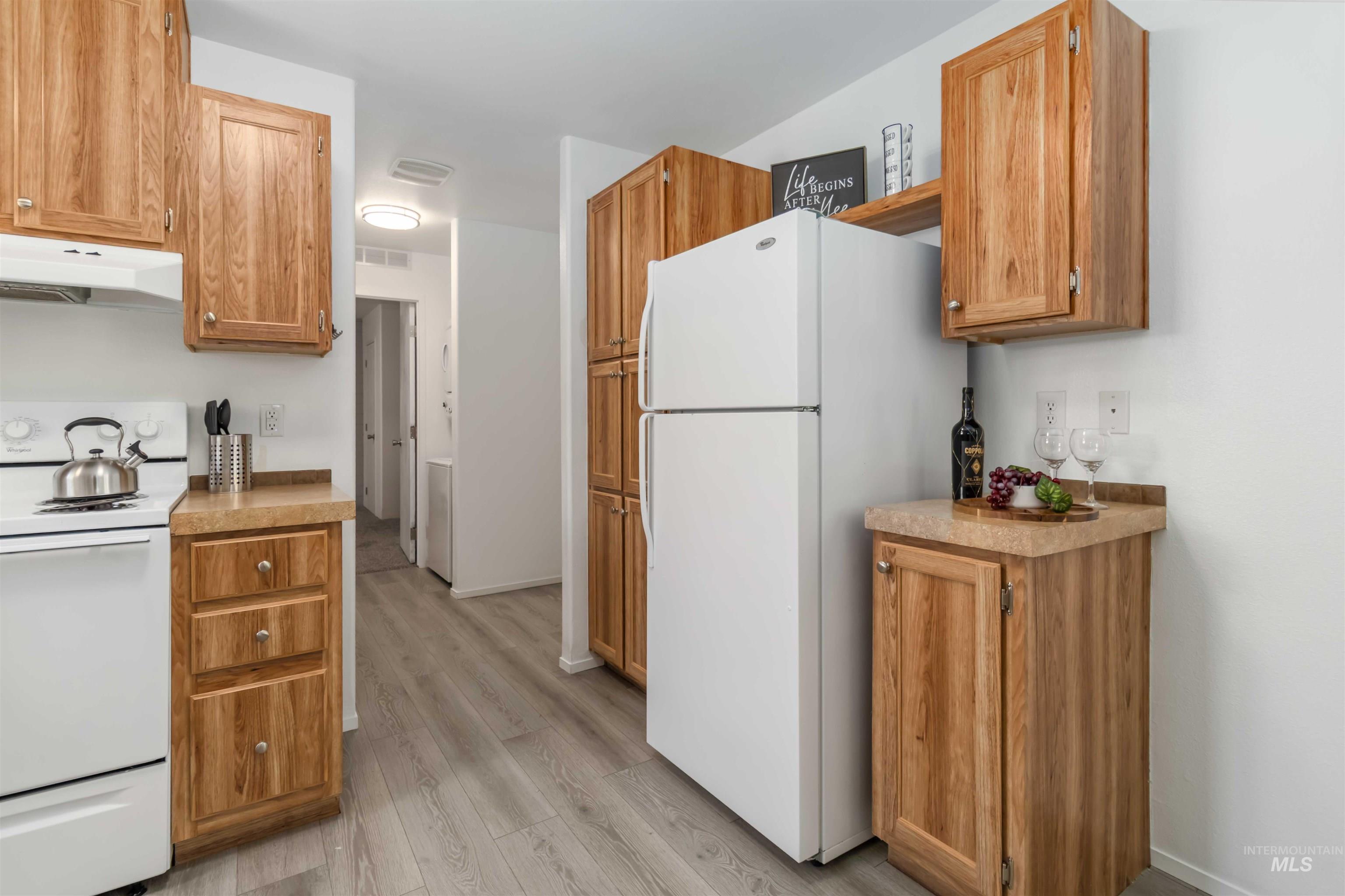 Kitchen featuring white appliances, light countertops, under cabinet range hood, and brown cabinetry