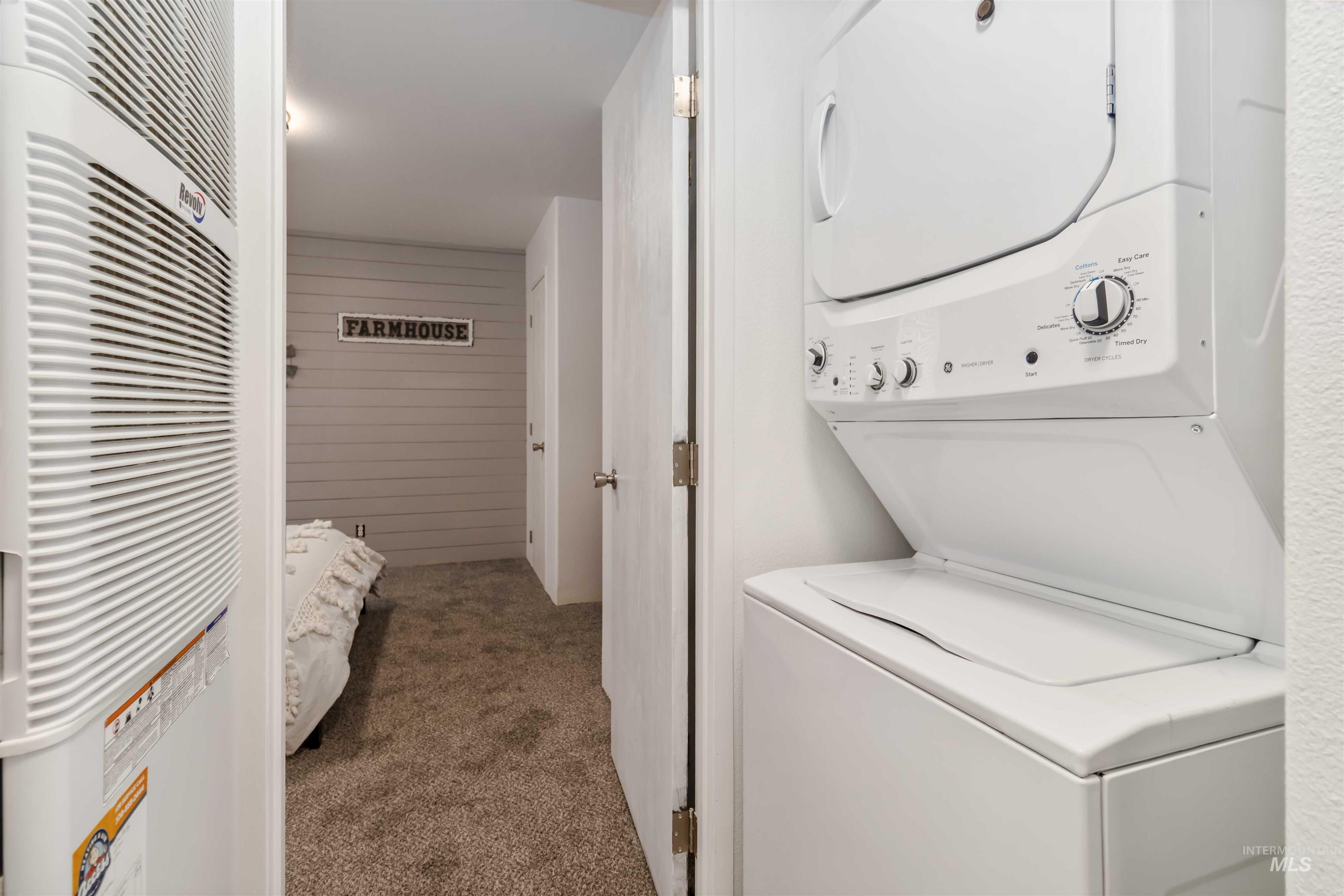 Laundry room featuring a heating unit, dark carpet, stacked washer / drying machine, and wooden walls