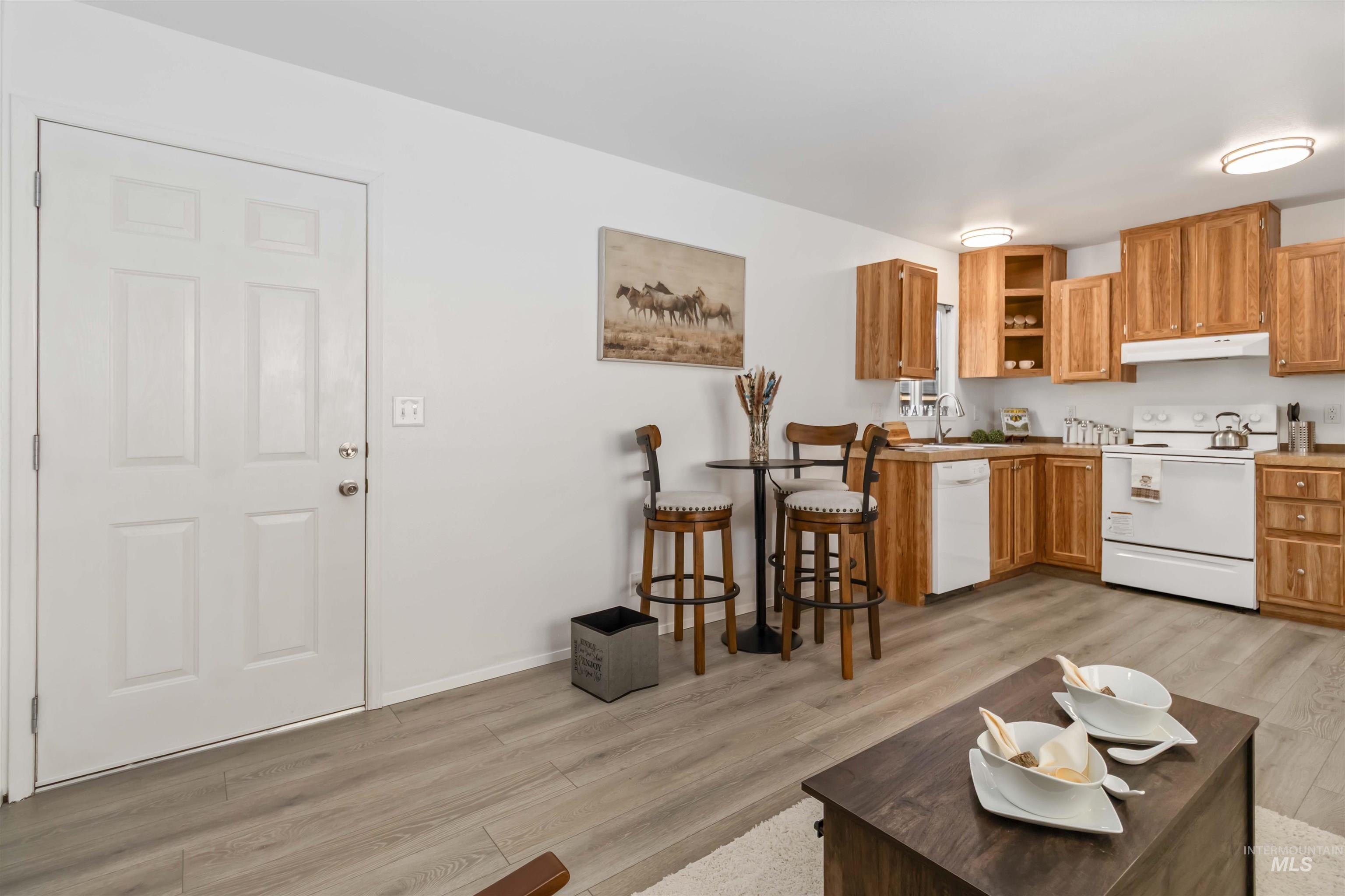 Kitchen featuring white appliances, light wood-style flooring, brown cabinets, and under cabinet range hood