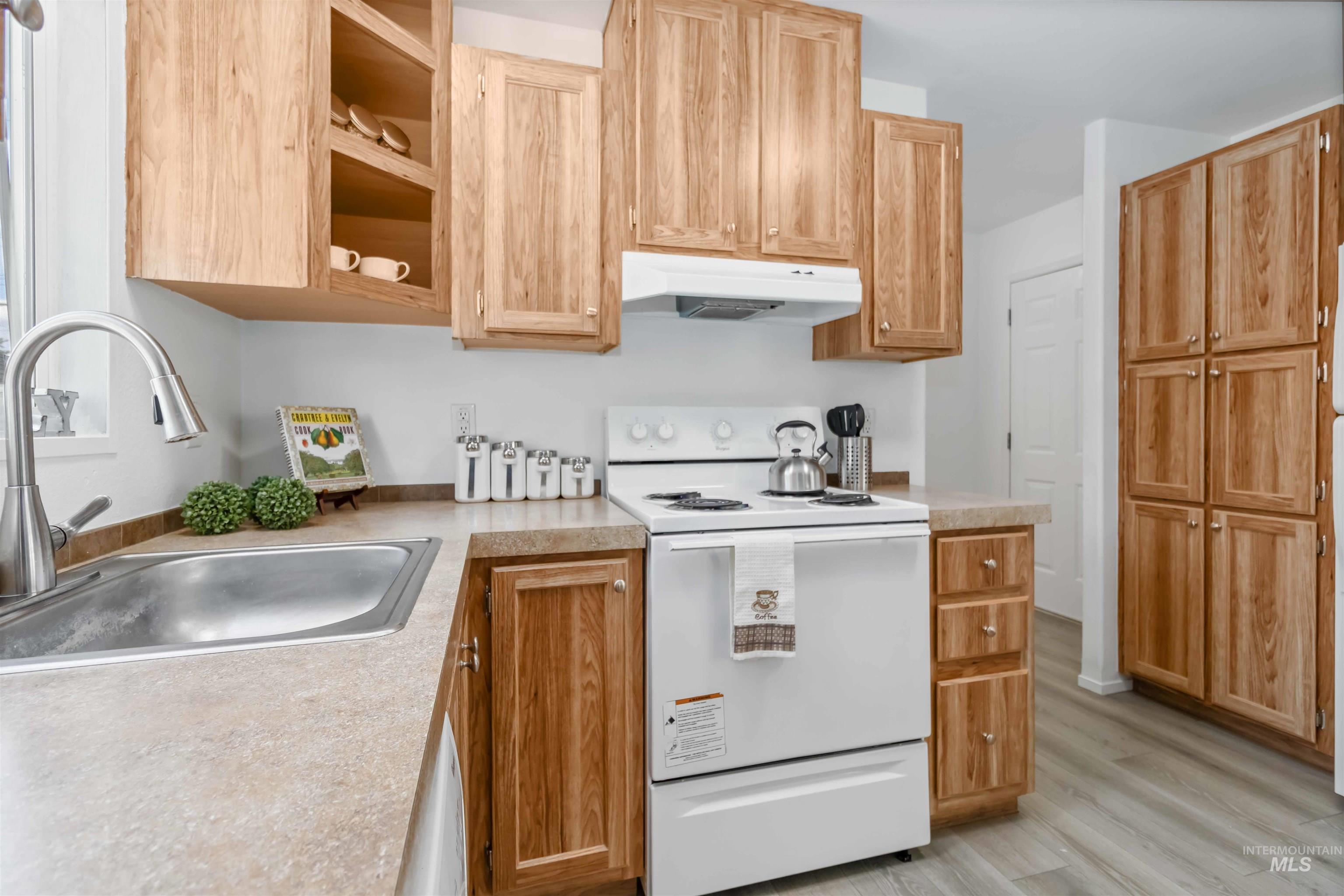 Kitchen featuring white range with electric stovetop, light countertops, under cabinet range hood, light wood-style flooring, and light brown cabinets