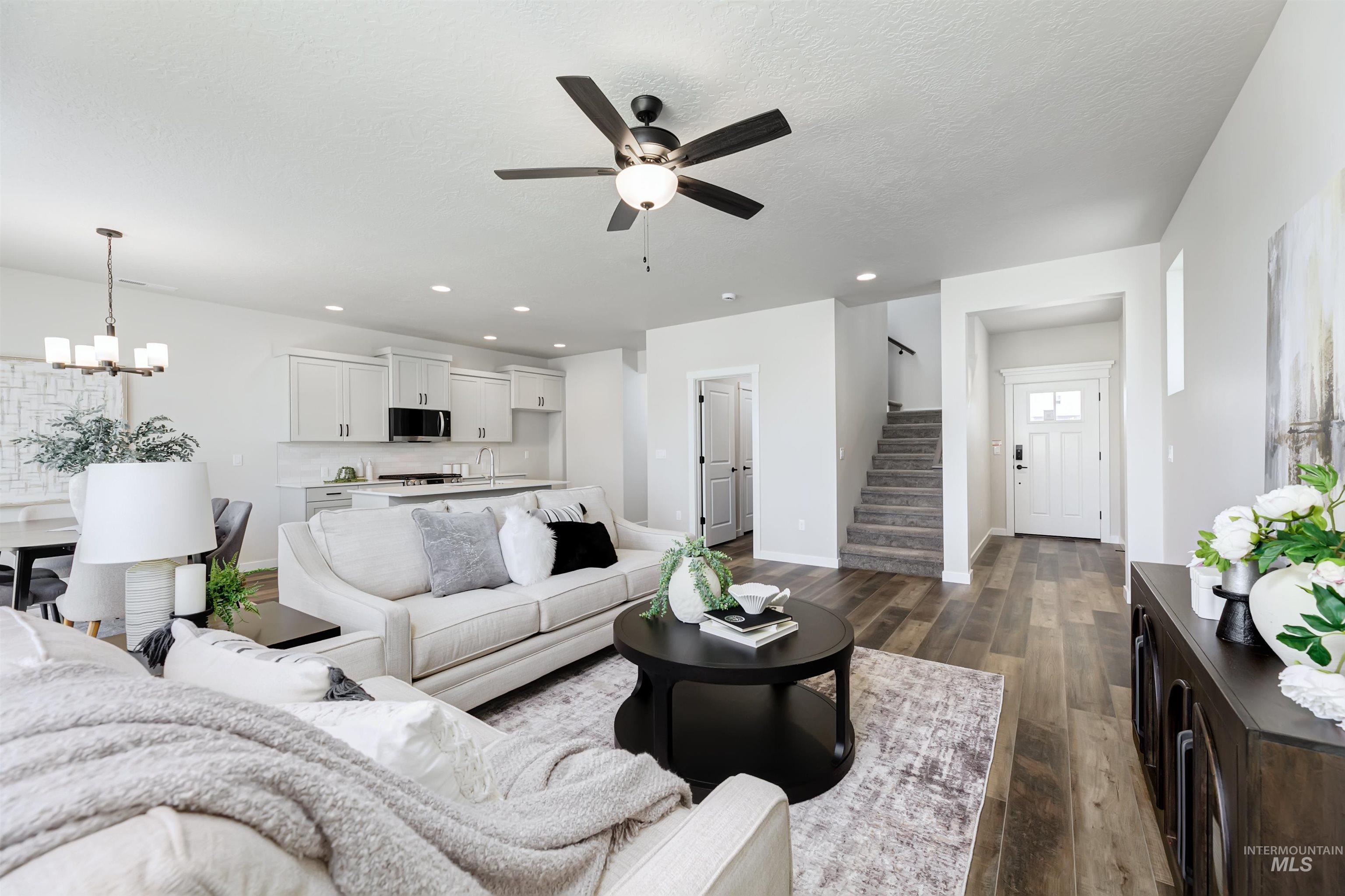 Living room with stairway, ceiling fan, a chandelier, dark wood-type flooring, and recessed lighting