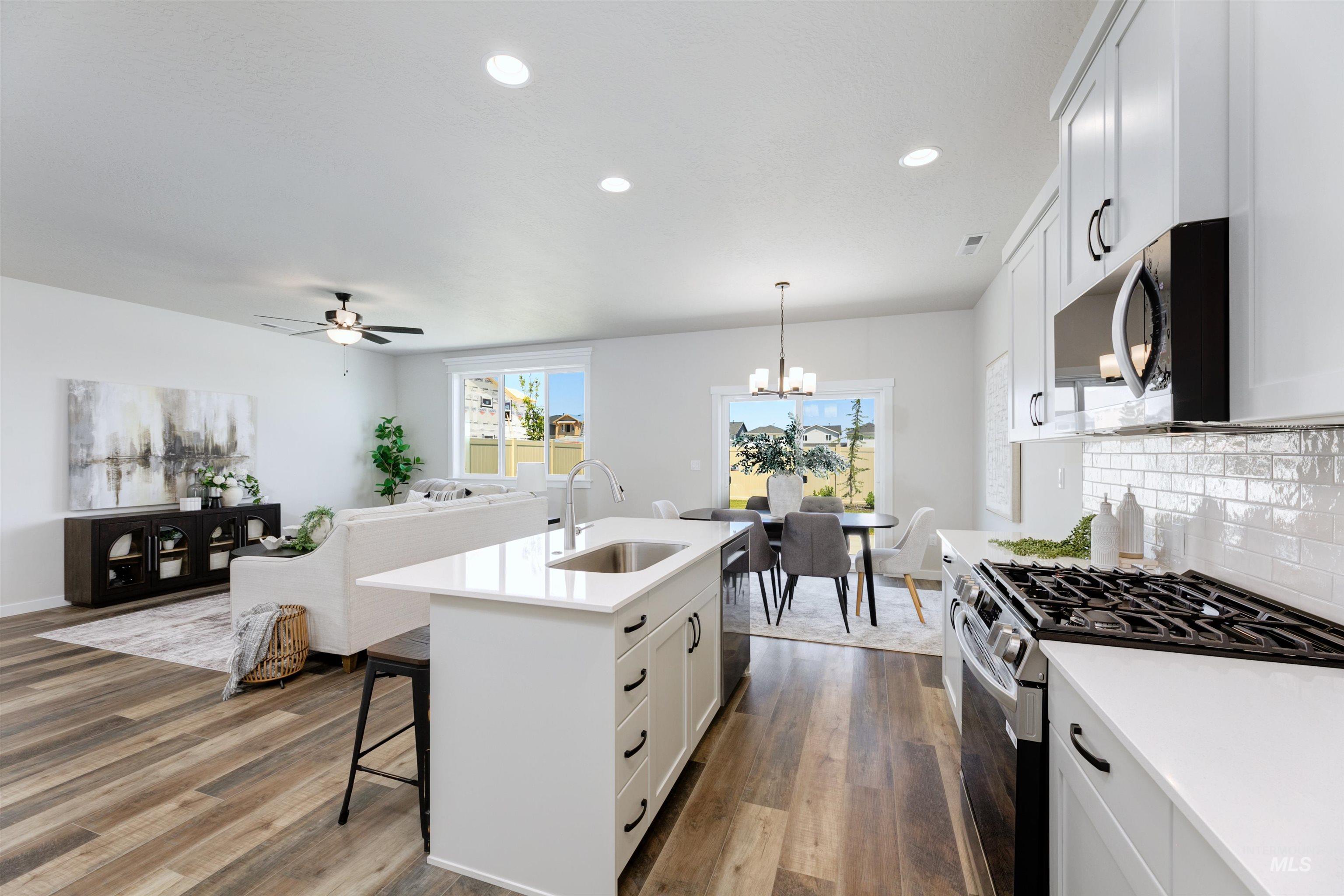 Kitchen with stainless steel appliances, wood finished floors, backsplash, white cabinets, and light countertops