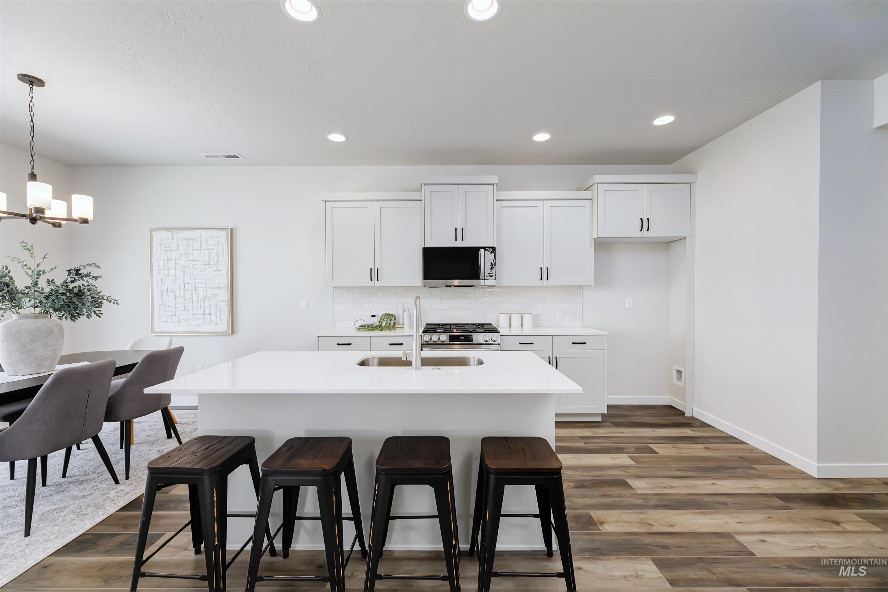 Kitchen with stainless steel appliances, a chandelier, a kitchen breakfast bar, dark wood-style floors, and recessed lighting