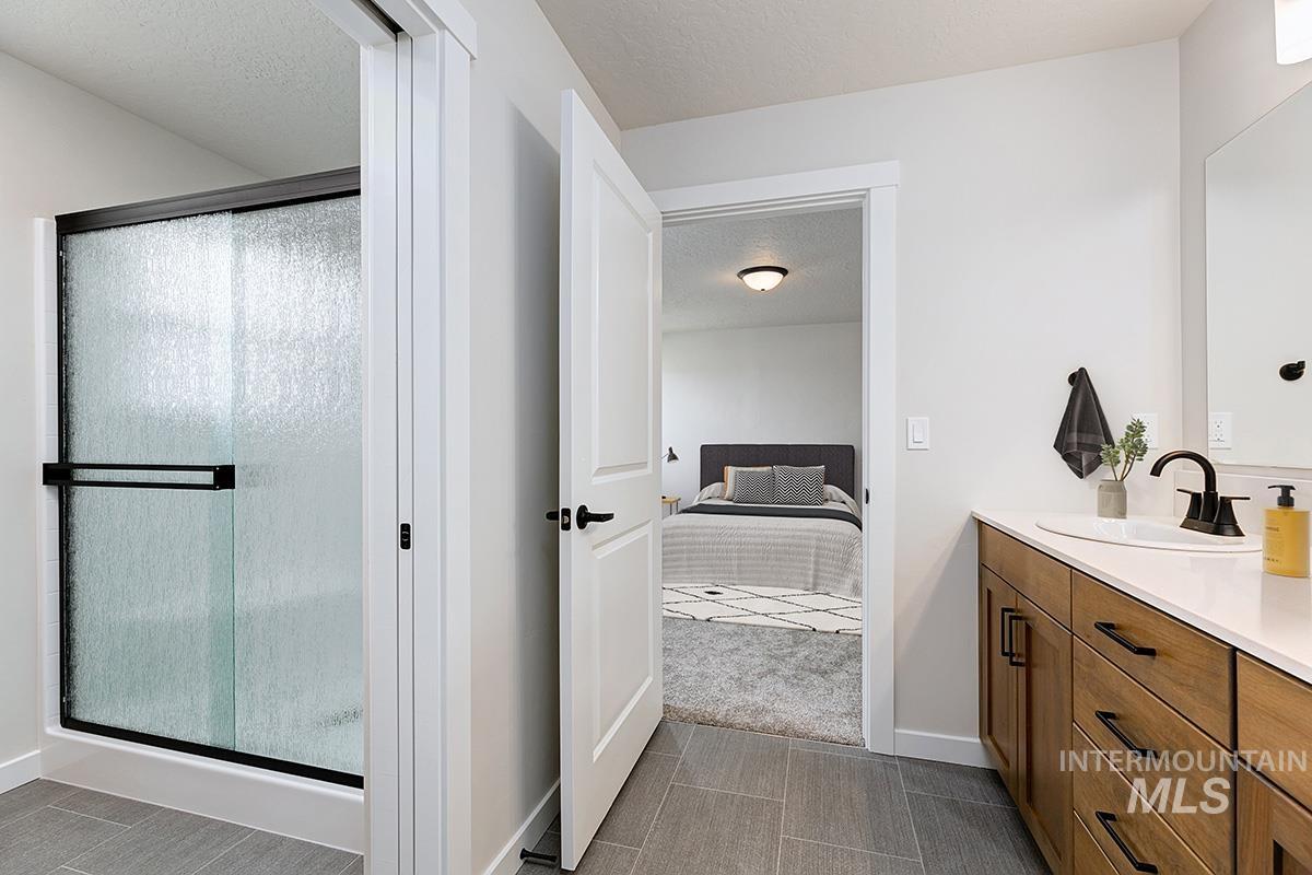 Full bathroom with vanity, ensuite bath, a textured ceiling, a stall shower, and dark tile patterned flooring