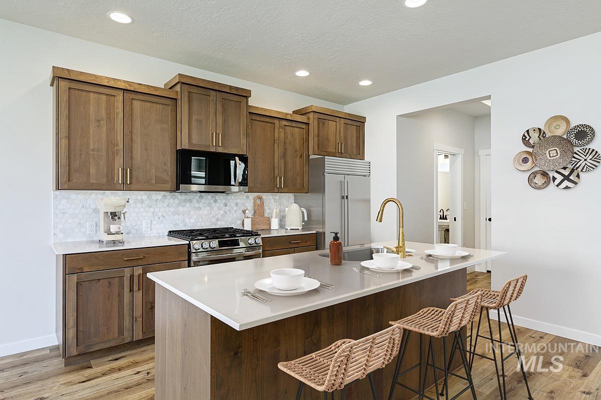 Kitchen with backsplash, an island with sink, light wood-type flooring, appliances with stainless steel finishes, and a breakfast bar area