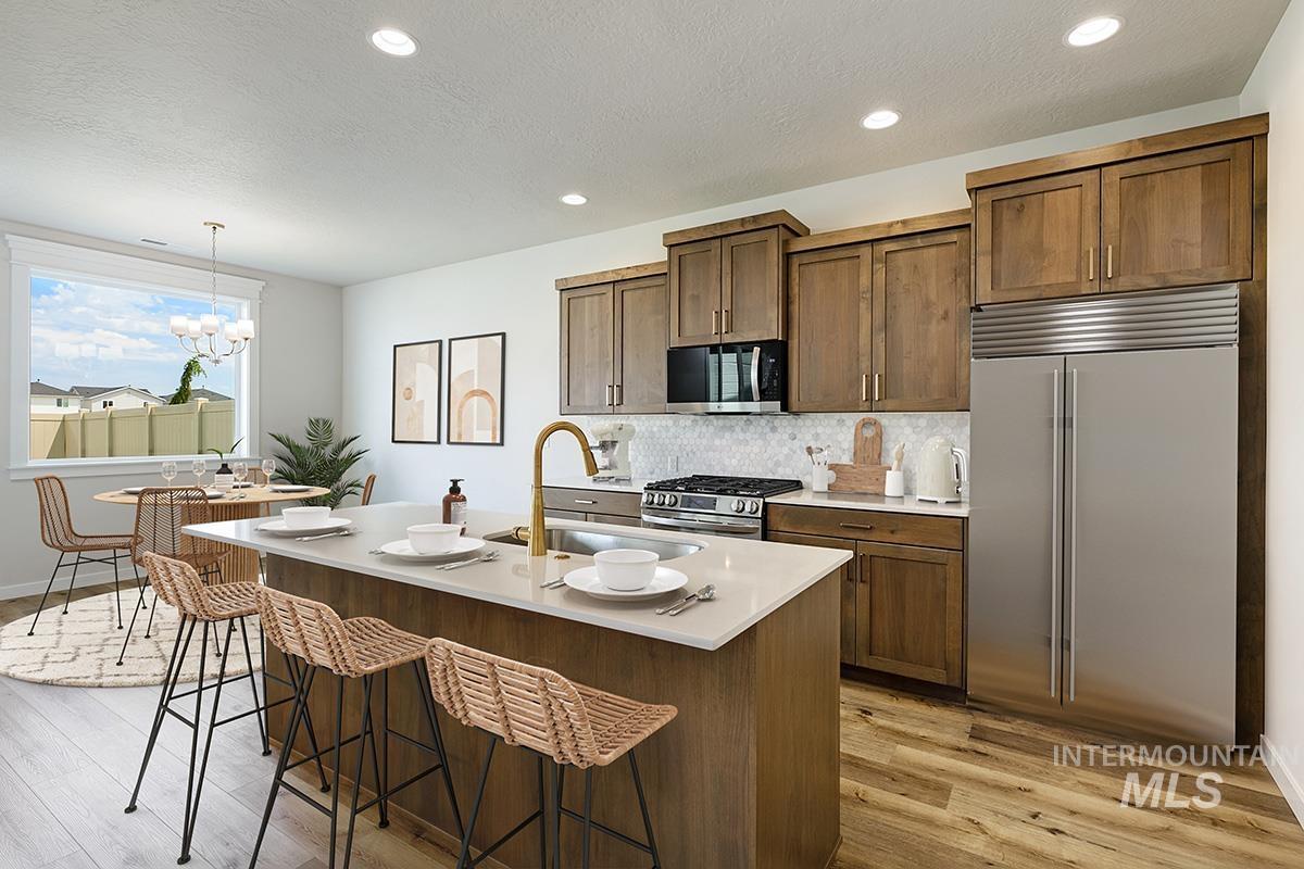 Kitchen featuring stainless steel appliances, decorative backsplash, a kitchen breakfast bar, brown cabinetry, and light wood-style floors
