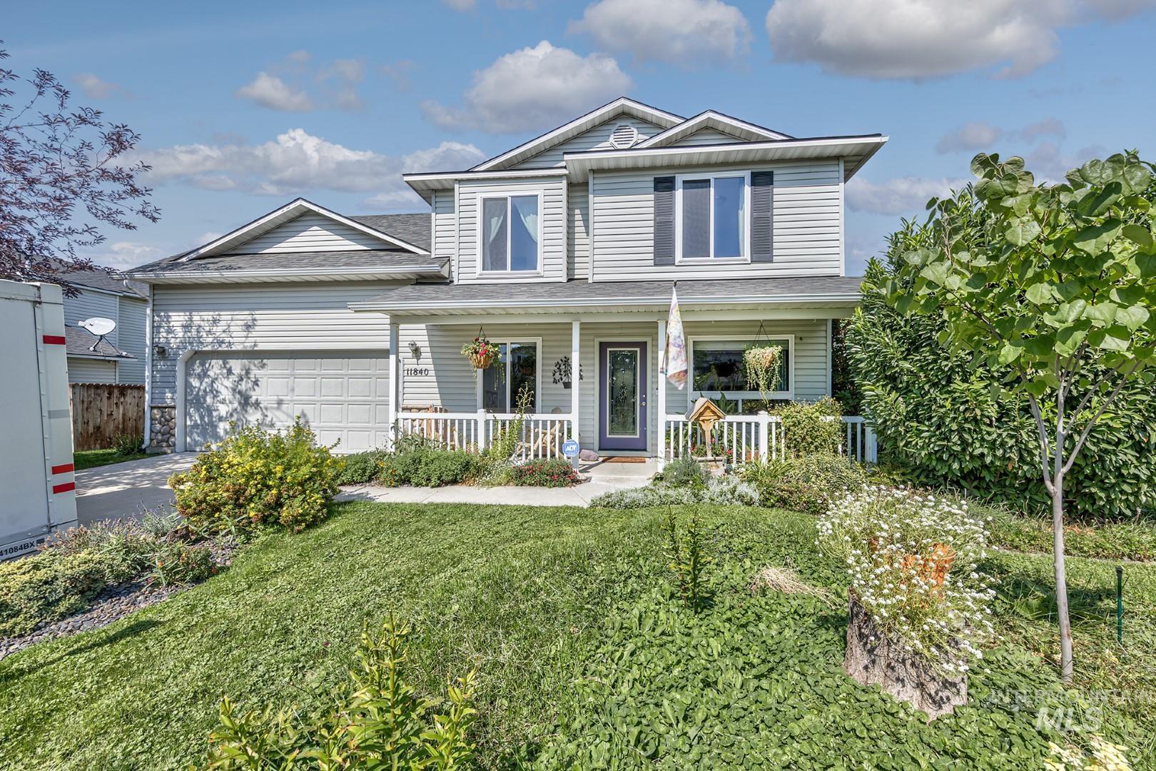 Traditional-style home with covered porch, an attached garage, driveway, roof with shingles, and a front yard