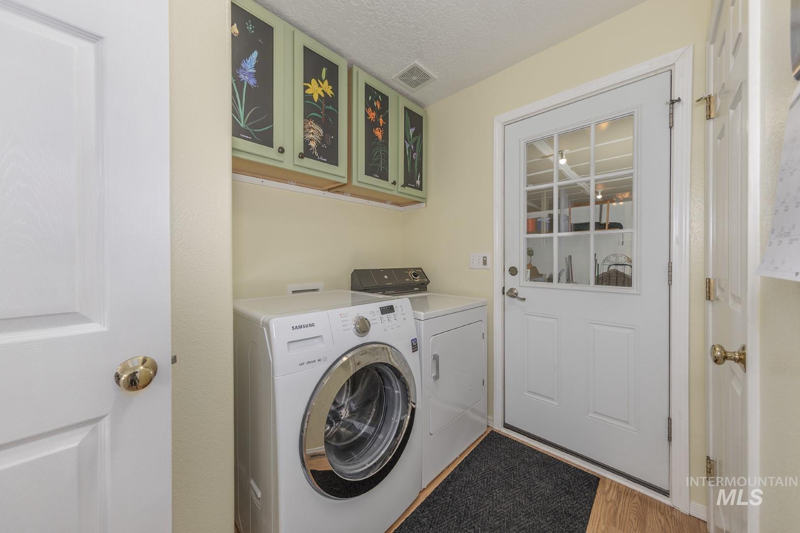 Laundry room with light wood finished floors, independent washer and dryer, a textured ceiling, and cabinet space