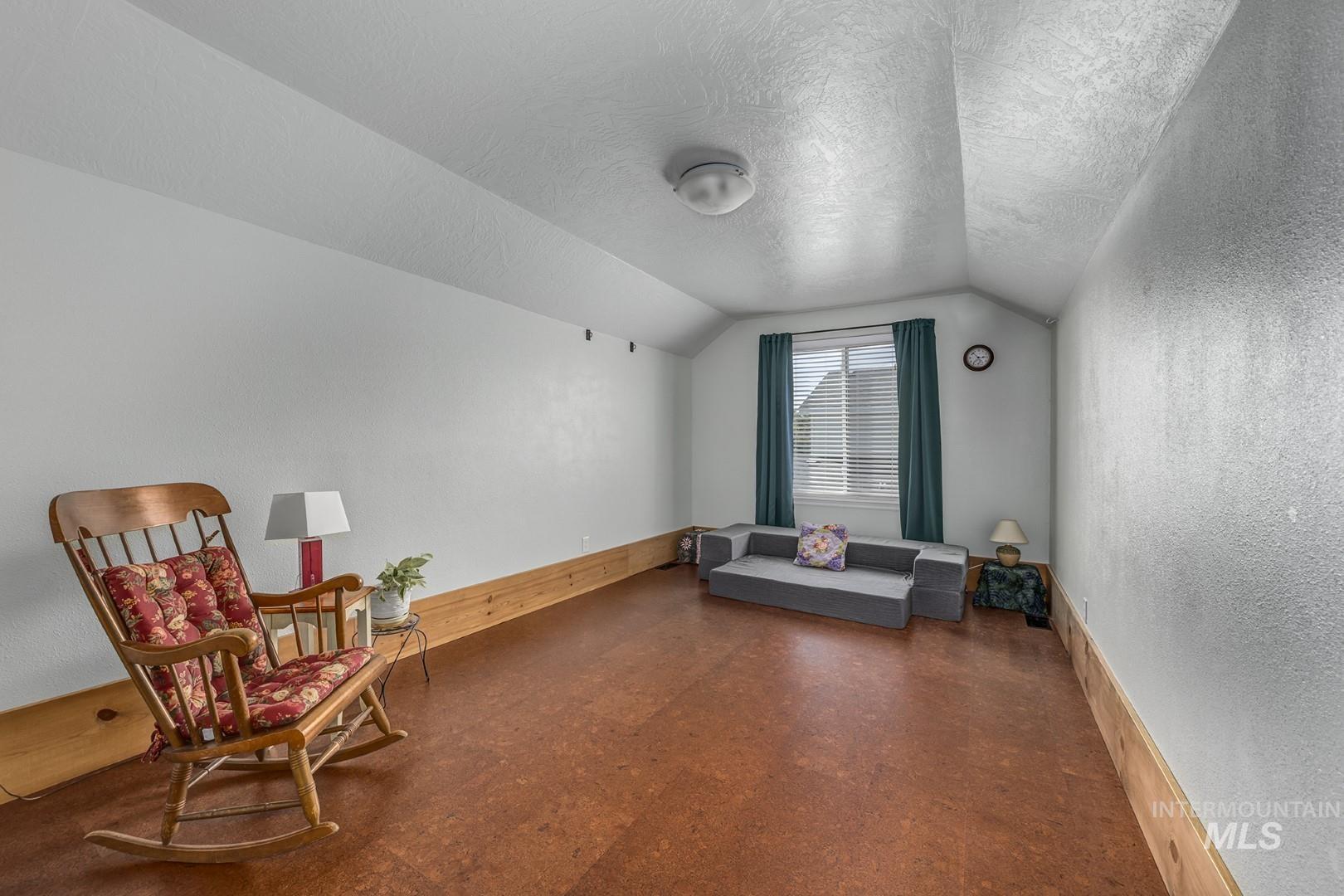 Living area featuring a textured ceiling, a textured wall, vaulted ceiling, and dark flooring
