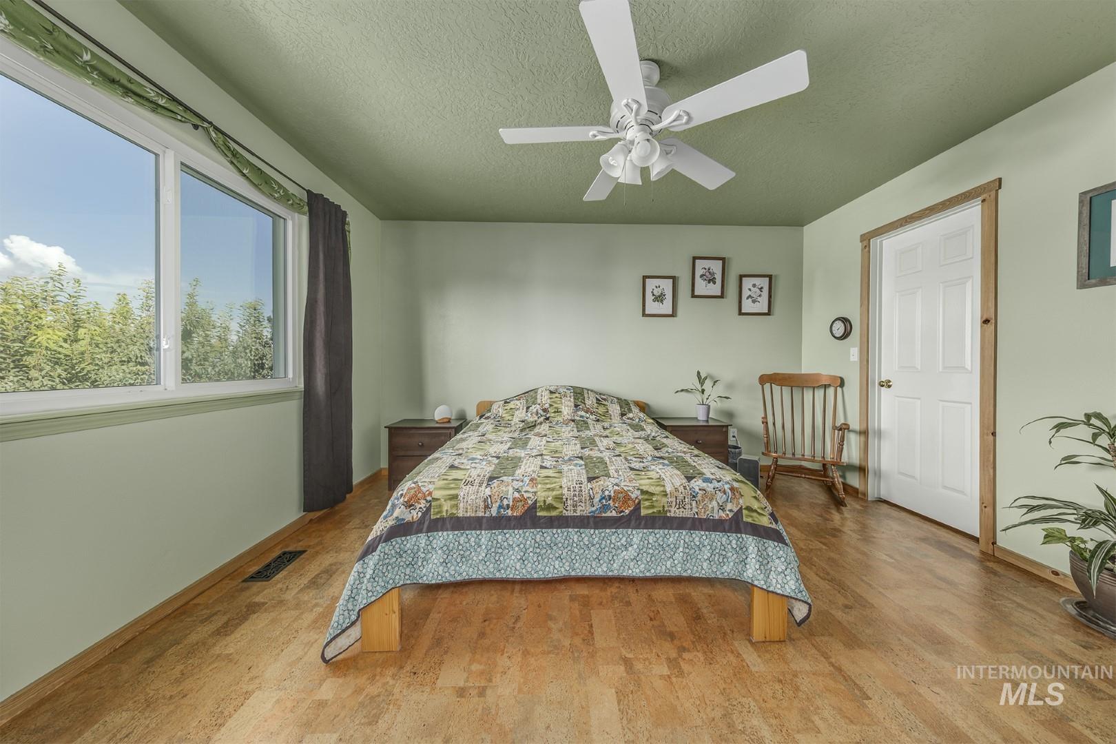 Bedroom with a textured ceiling, wood finished floors, and a ceiling fan