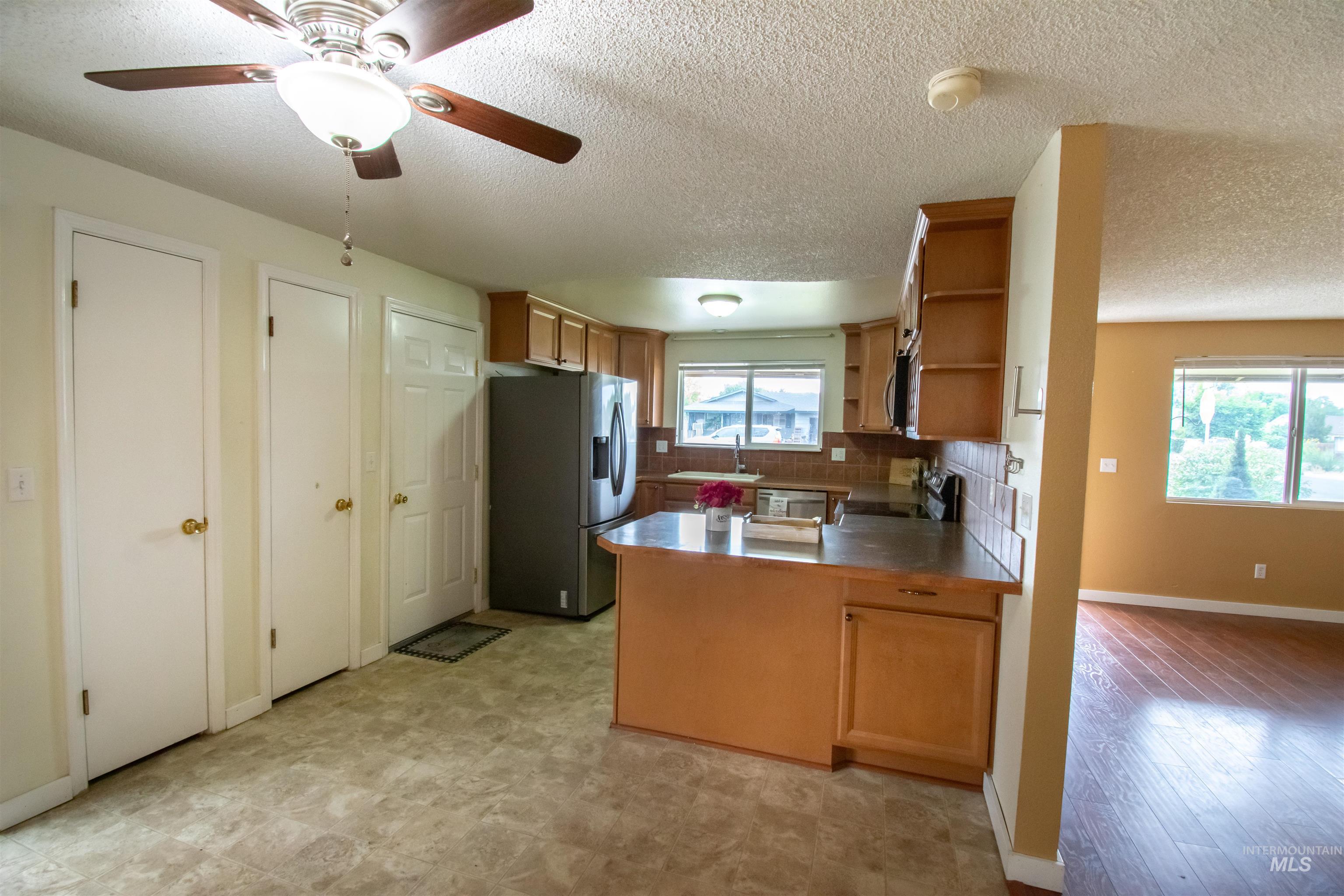 Kitchen with stainless steel refrigerator with ice dispenser, a peninsula, a textured ceiling, open shelves, and backsplash