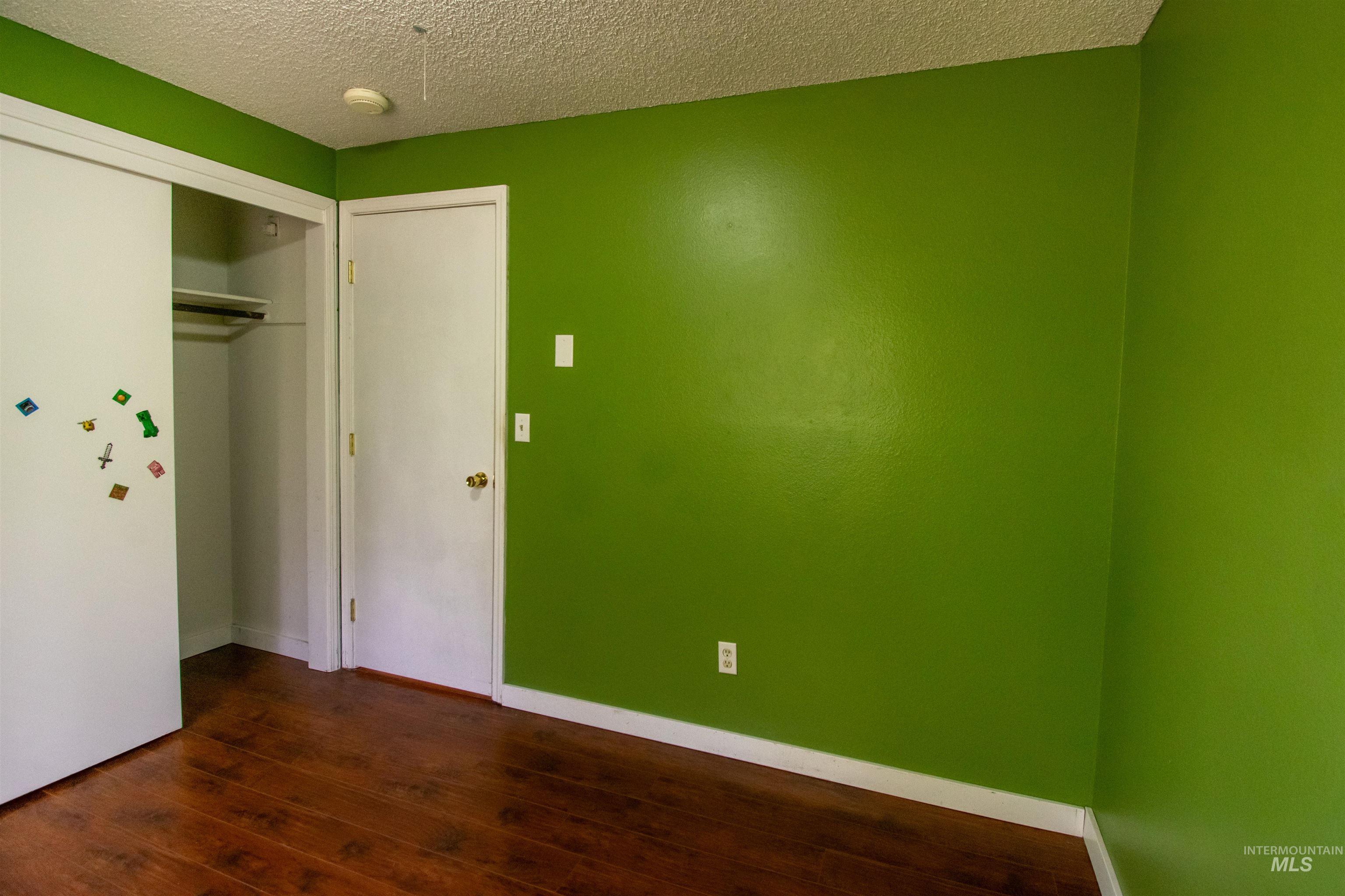 Unfurnished bedroom with a textured ceiling, dark wood-style flooring, and a closet