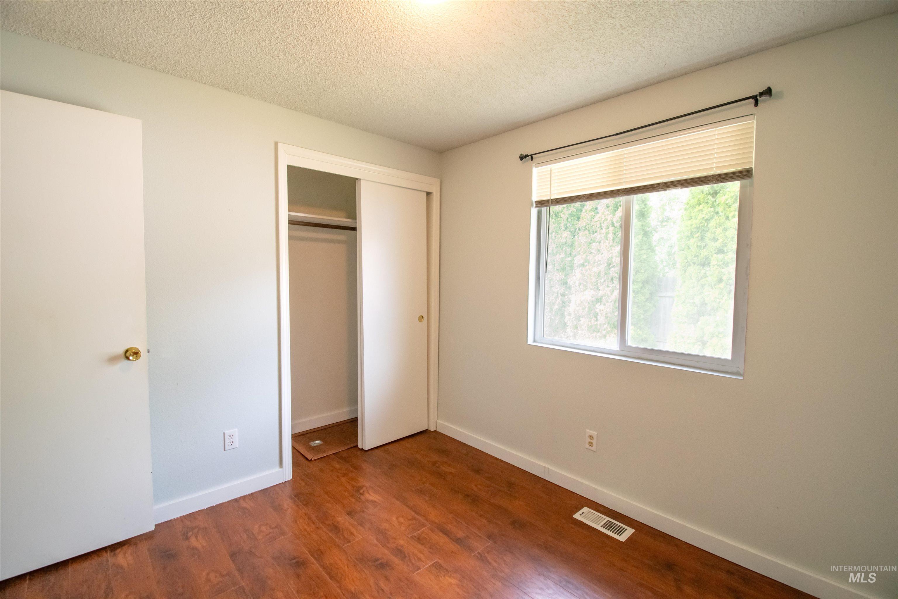 Unfurnished bedroom featuring a textured ceiling, dark wood-type flooring, and a closet