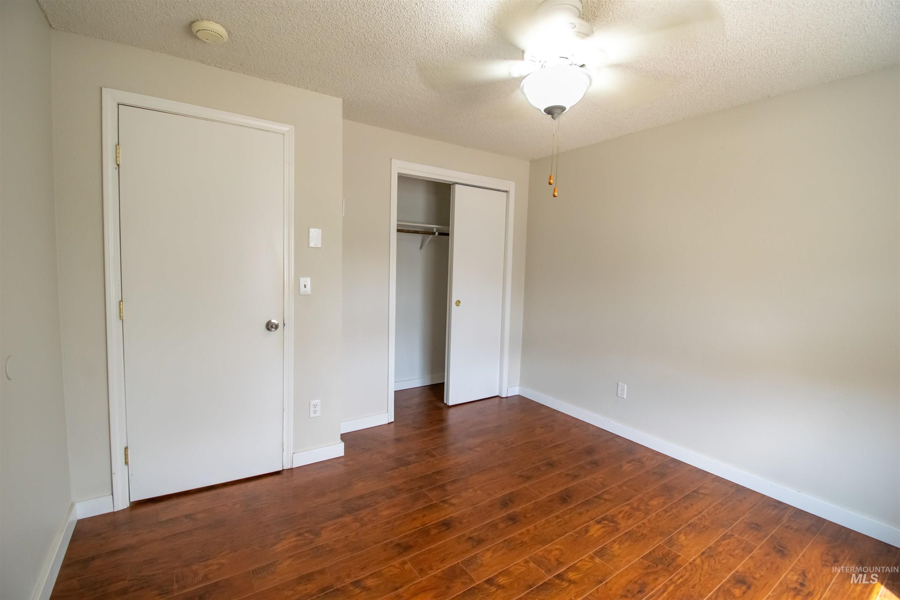 Unfurnished bedroom featuring a textured ceiling, a closet, dark wood-style flooring, and a ceiling fan