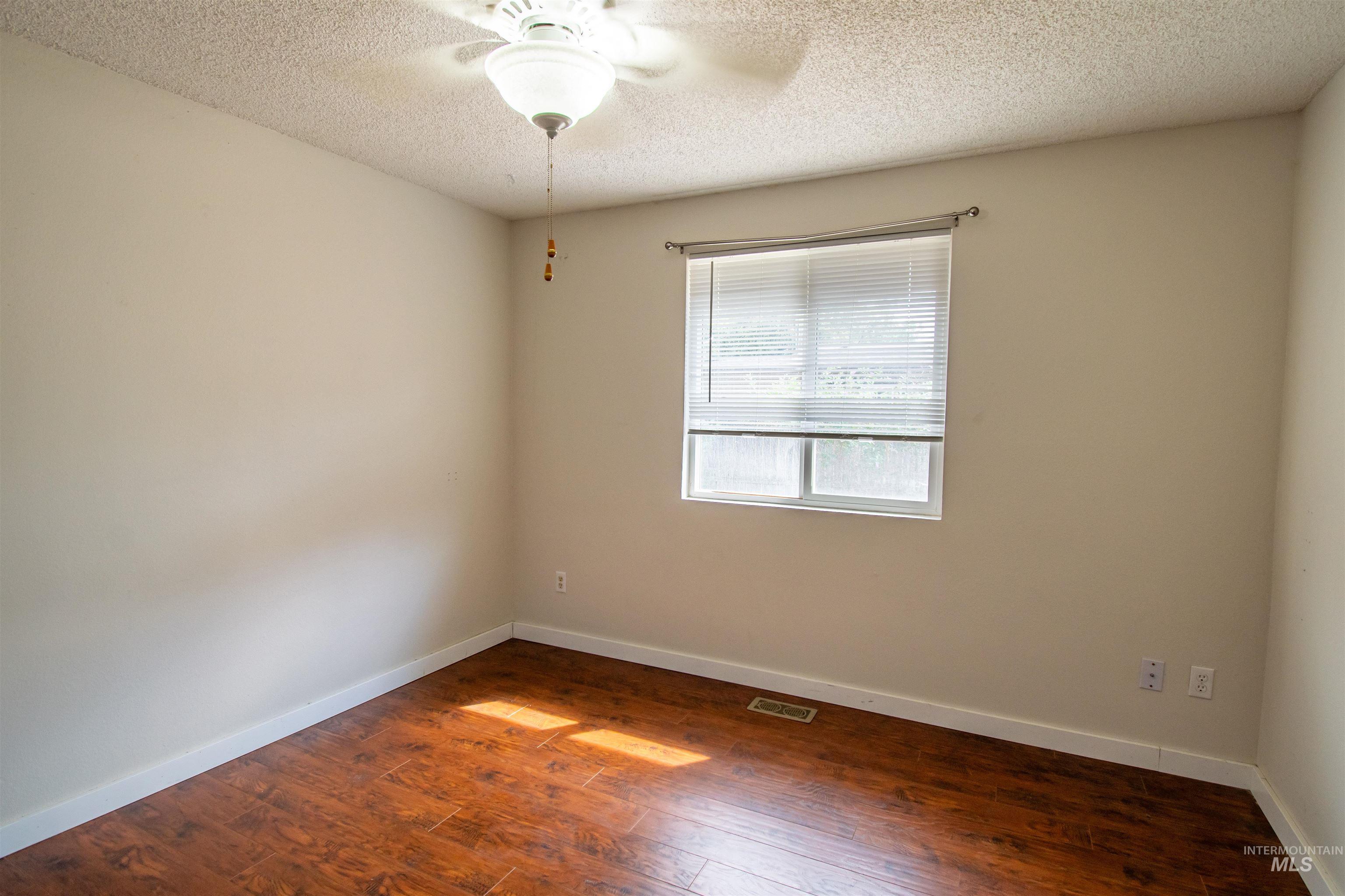 Spare room with dark wood-style flooring, a textured ceiling, and a ceiling fan
