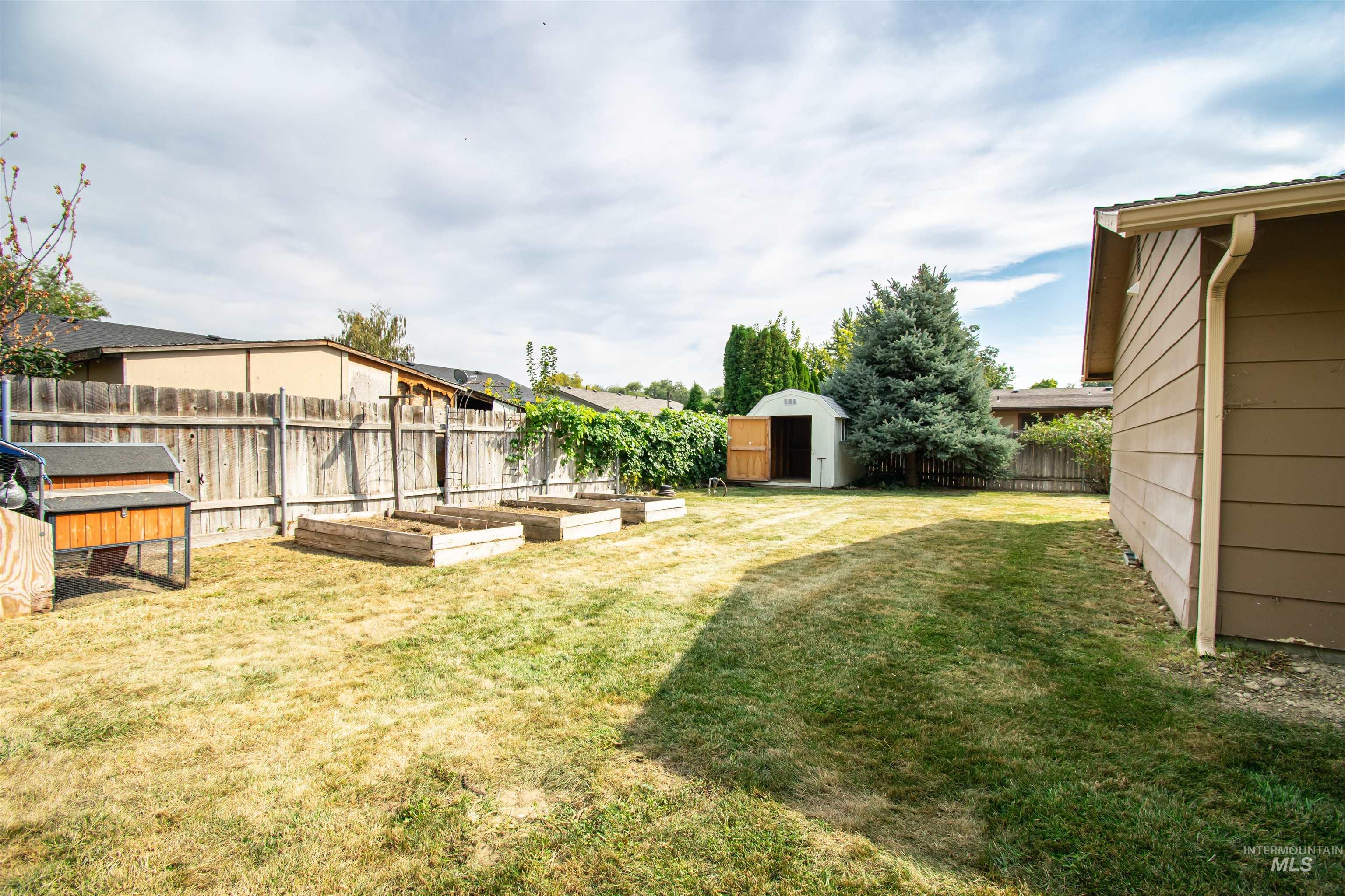 Fenced backyard featuring a storage unit and a garden
