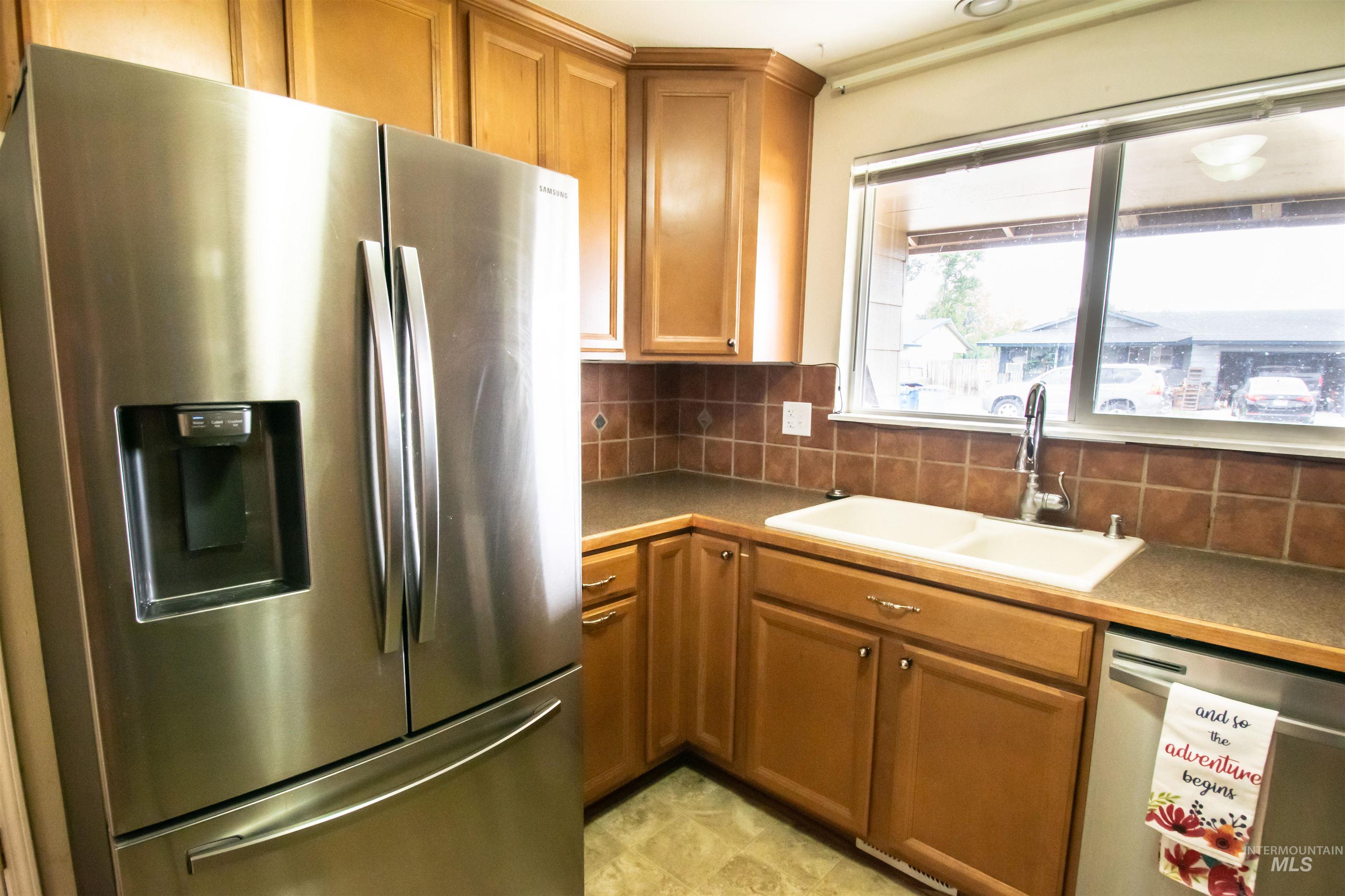 Kitchen with appliances with stainless steel finishes, tasteful backsplash, brown cabinetry, and dark countertops