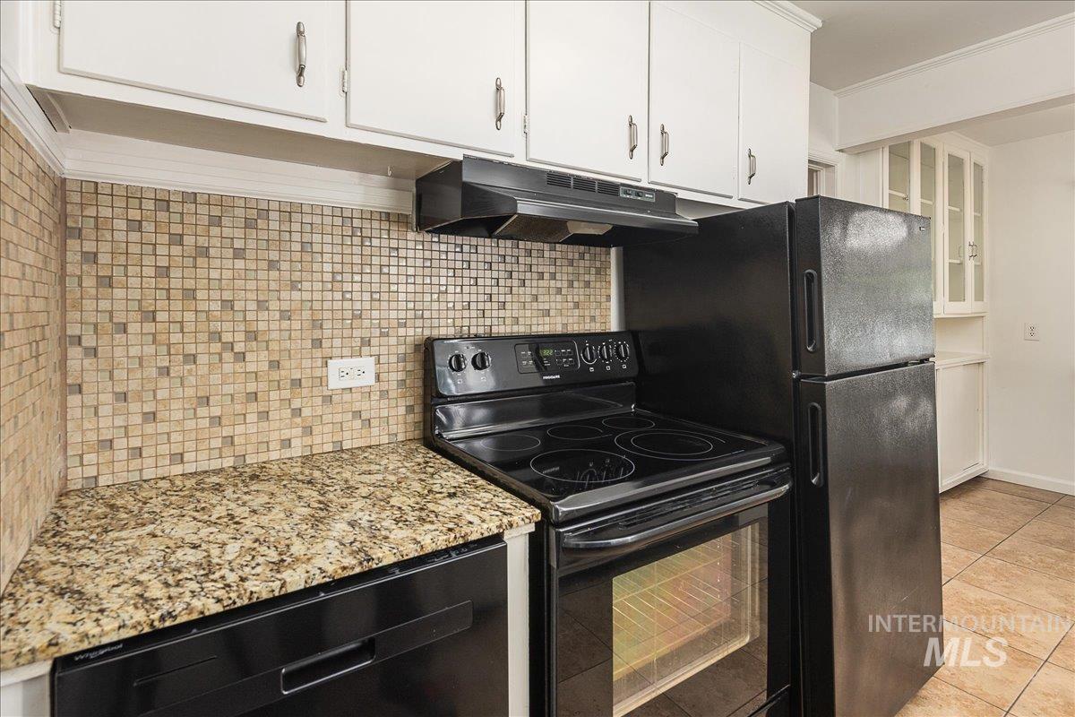 Kitchen featuring decorative backsplash, black appliances, under cabinet range hood, light tile patterned floors, and white cabinets