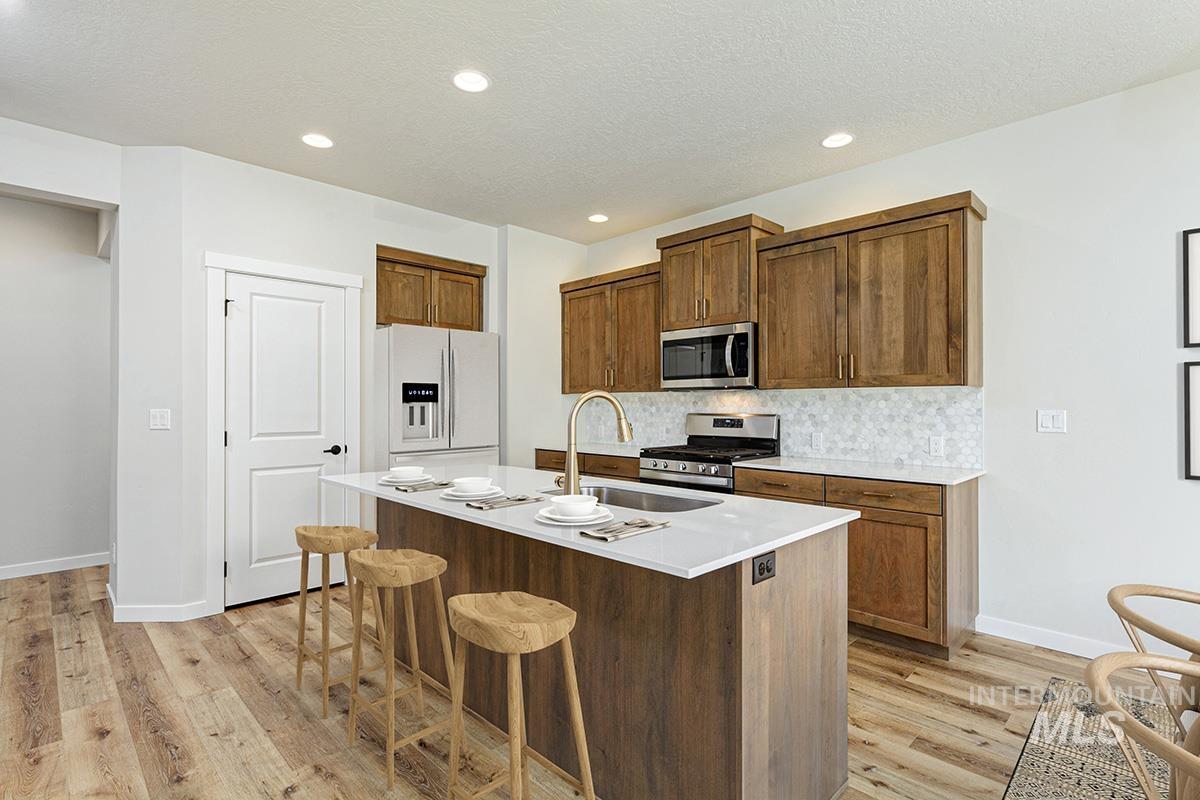 Kitchen with a breakfast bar area, appliances with stainless steel finishes, a center island with sink, brown cabinetry, and a textured ceiling