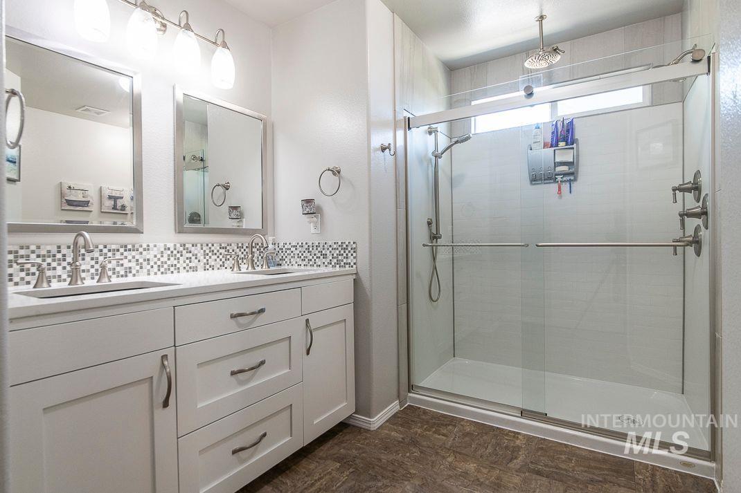 Full bath featuring a stall shower, backsplash, and double vanity