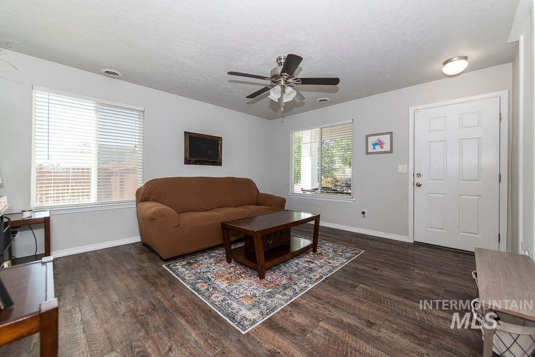 Living room with a textured ceiling, dark wood-style flooring, and ceiling fan