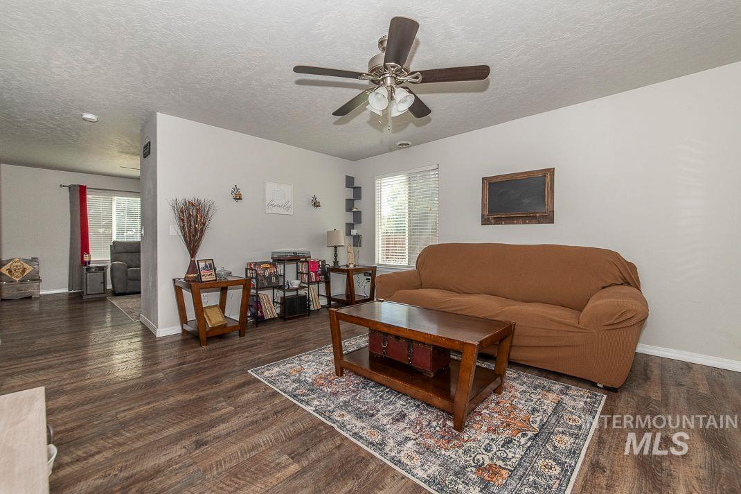 Living room with a textured ceiling, dark wood-style floors, and a ceiling fan