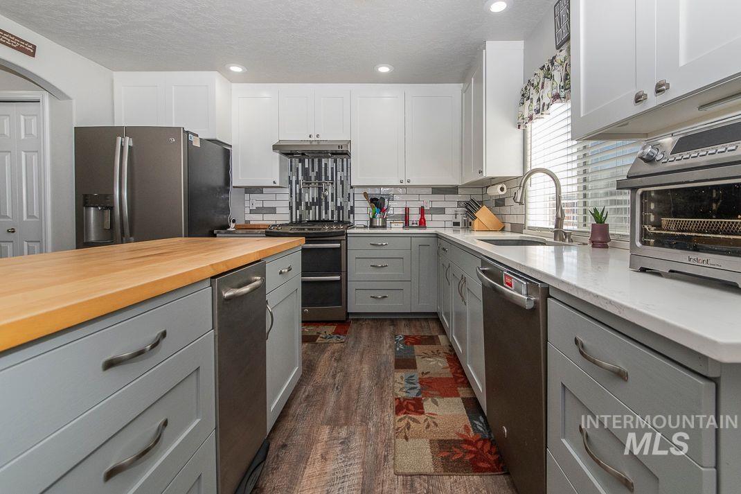 Kitchen with custom gray cabinetry, stainless steel appliances, dark wood lvp floors and full tile backsplash