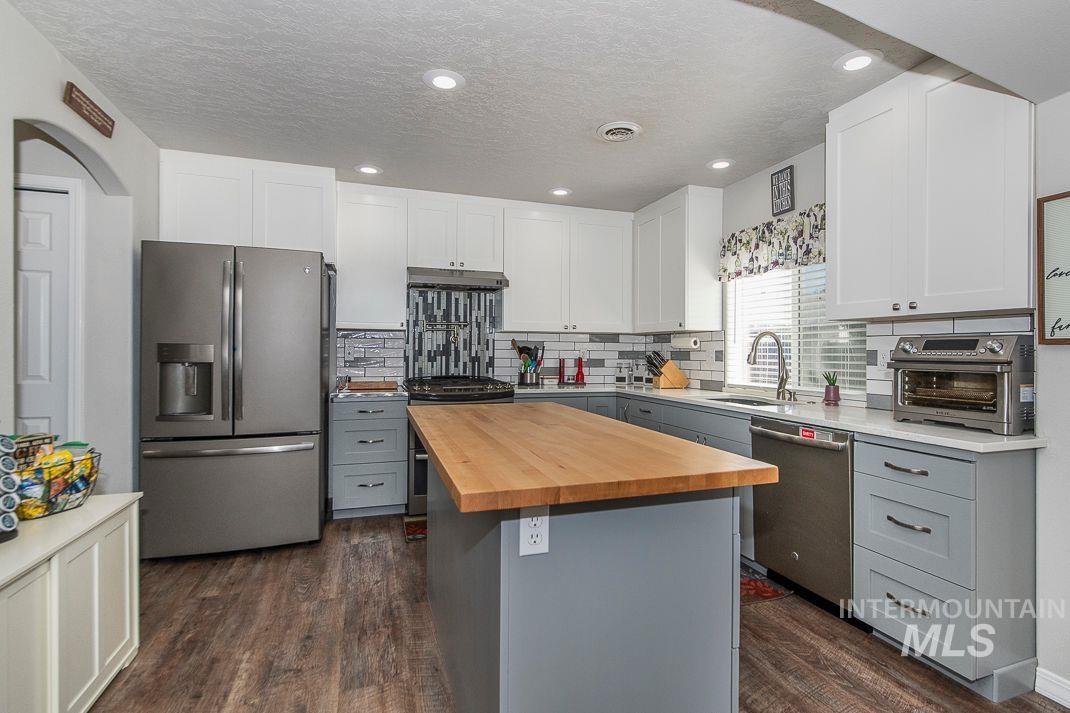 Kitchen featuring gray cabinetry, appliances with stainless steel finishes, a kitchen island, dark lvp floors, and backsplash