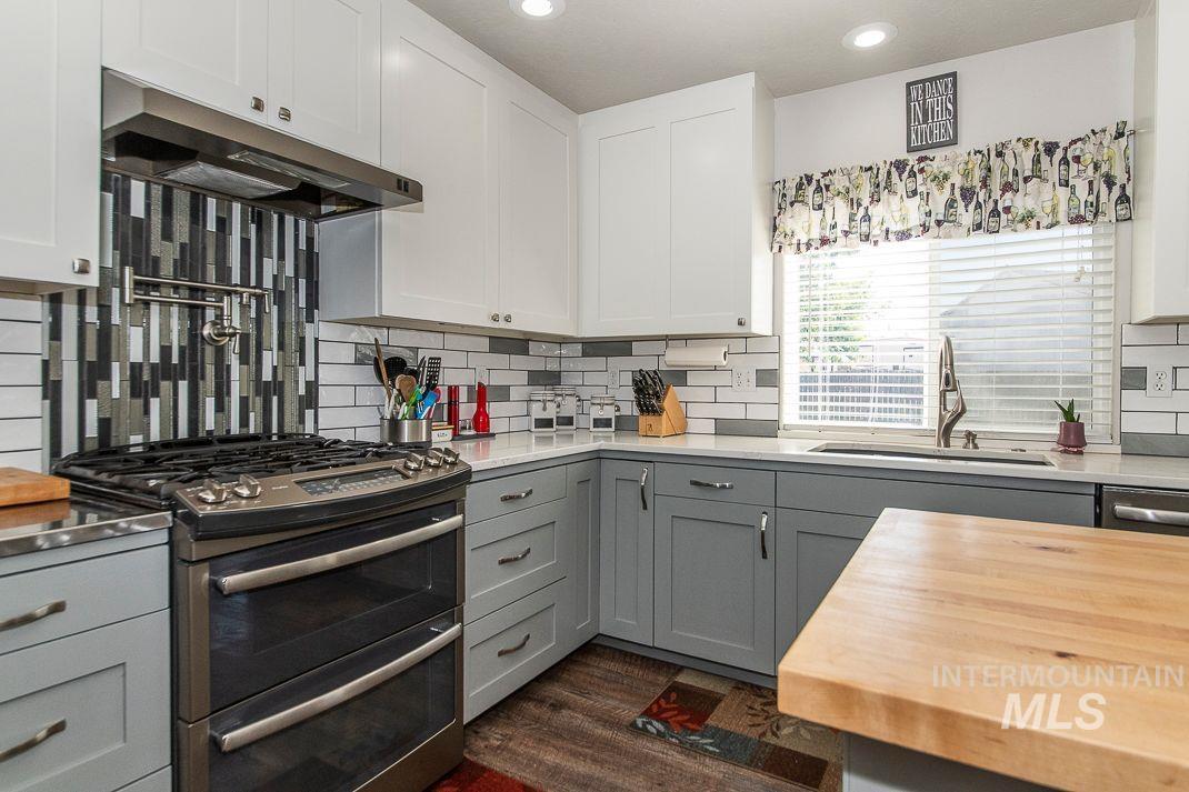 Kitchen featuring gray cabinets, double oven range, under cabinet range hood, quartz countertops and butcher block kitchen island, and full tile backsplash