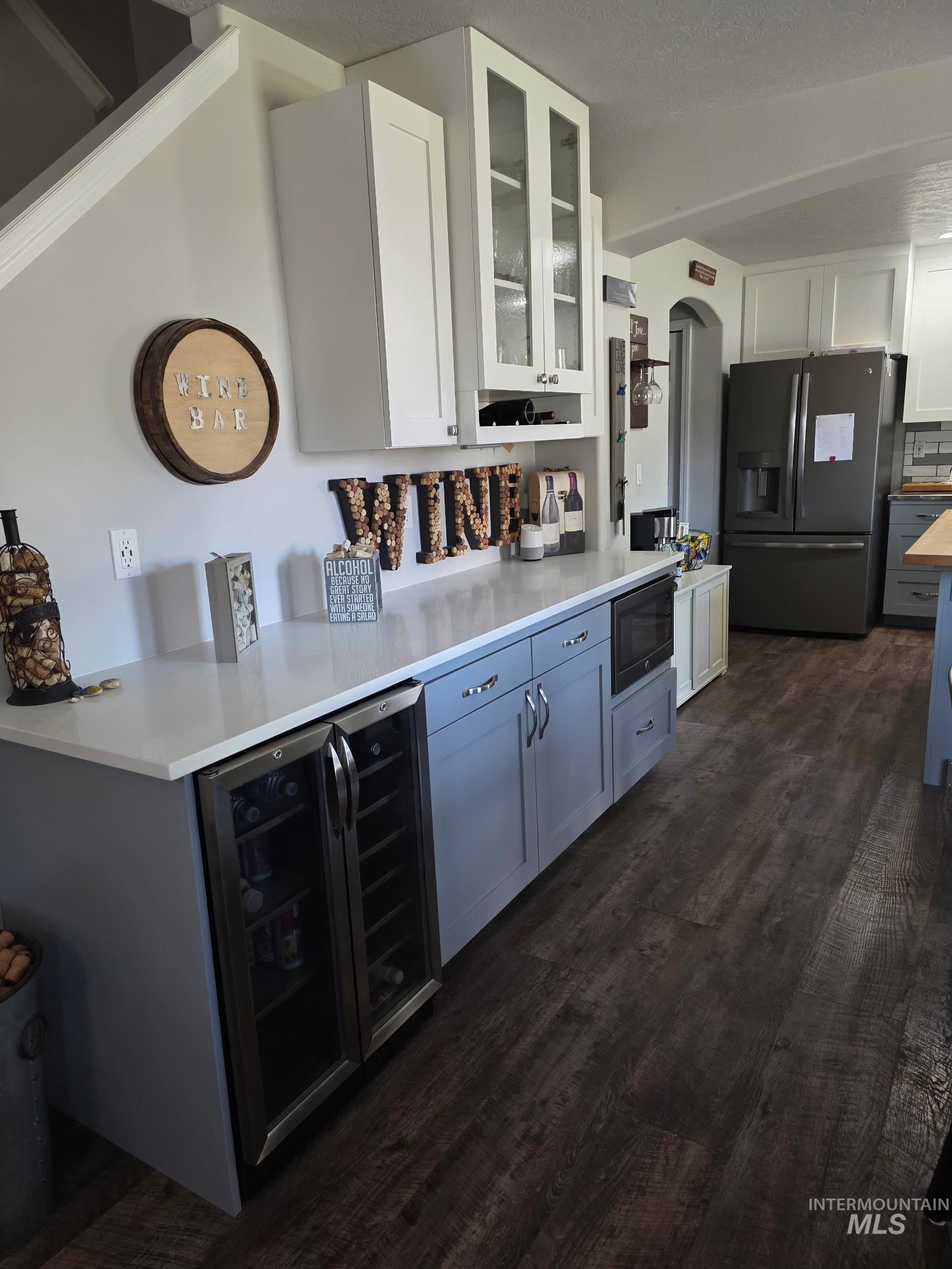 Bar area with white cabinetry, stainless steel fridge, glass insert cabinets, and beverage cooler