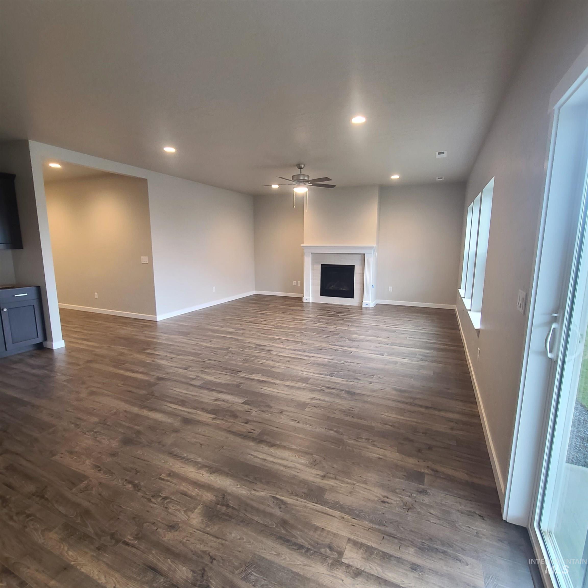 Unfurnished living room with recessed lighting, ceiling fan, a fireplace, and dark wood-style flooring