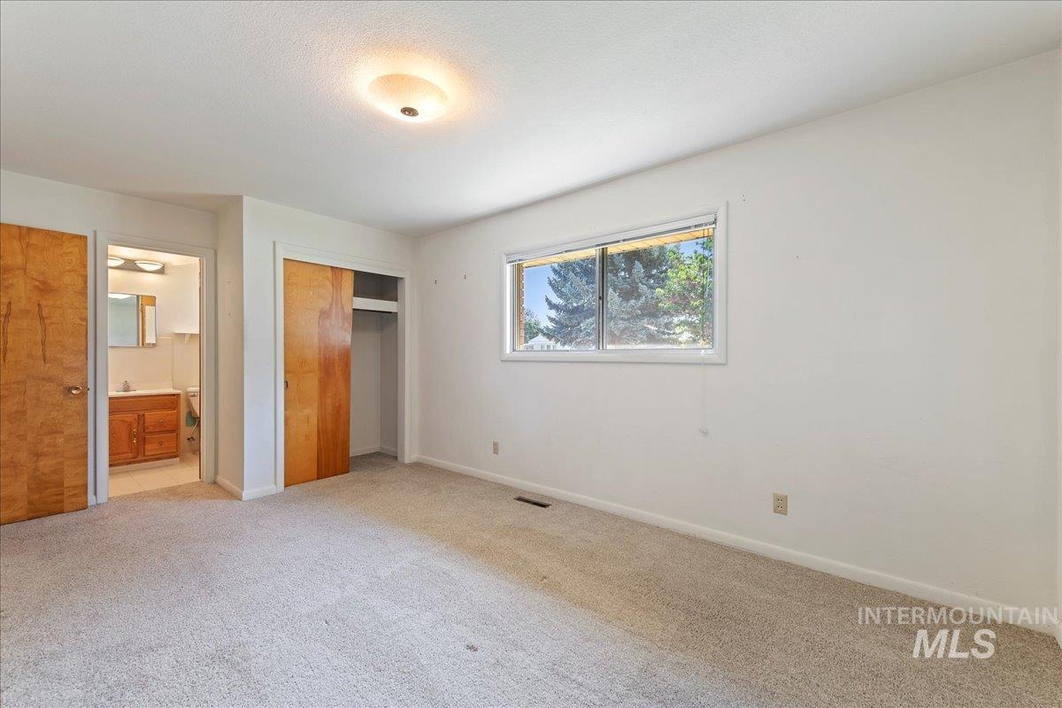 Unfurnished bedroom featuring a closet, light colored carpet, and connected bathroom