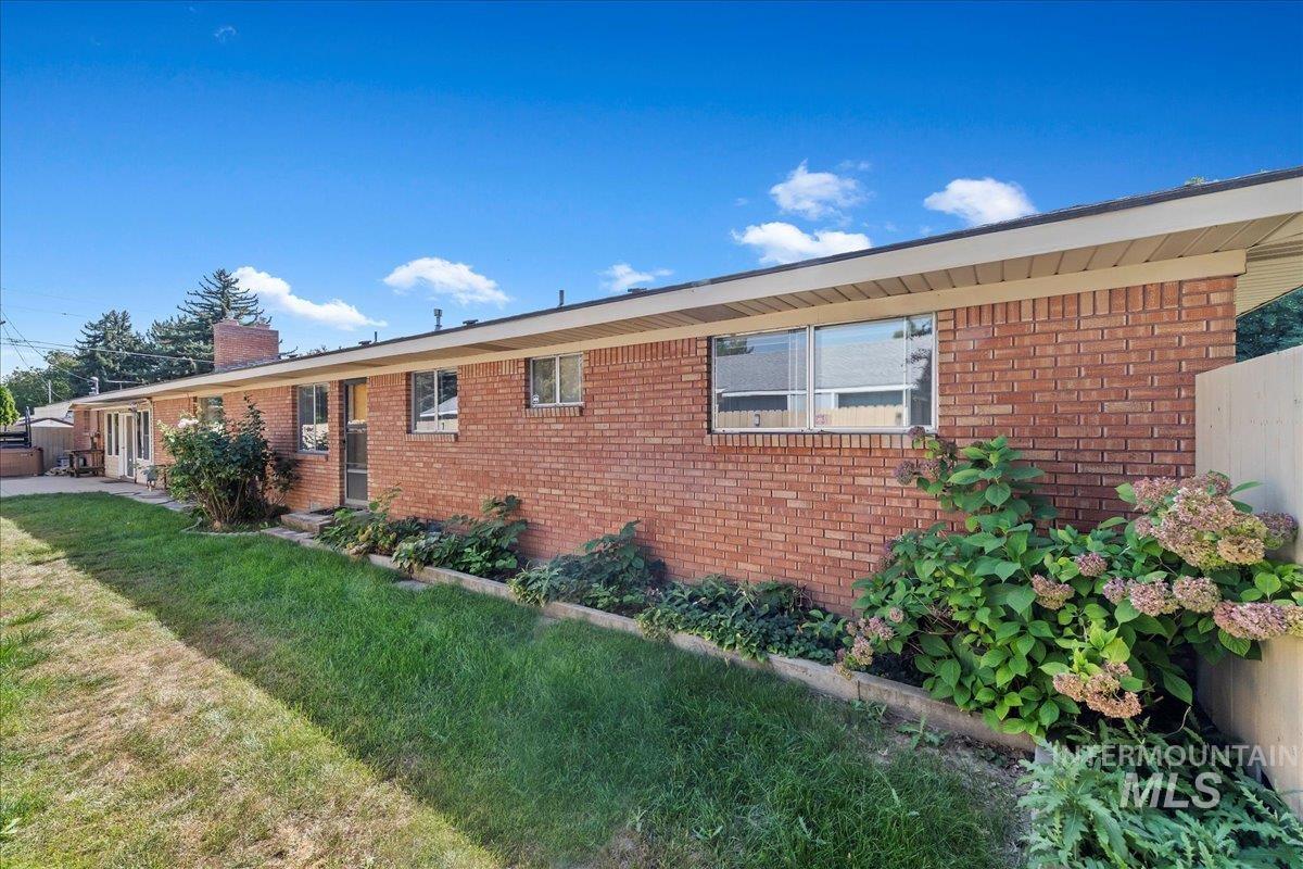 View of side of home with brick siding, a chimney, and a lawn