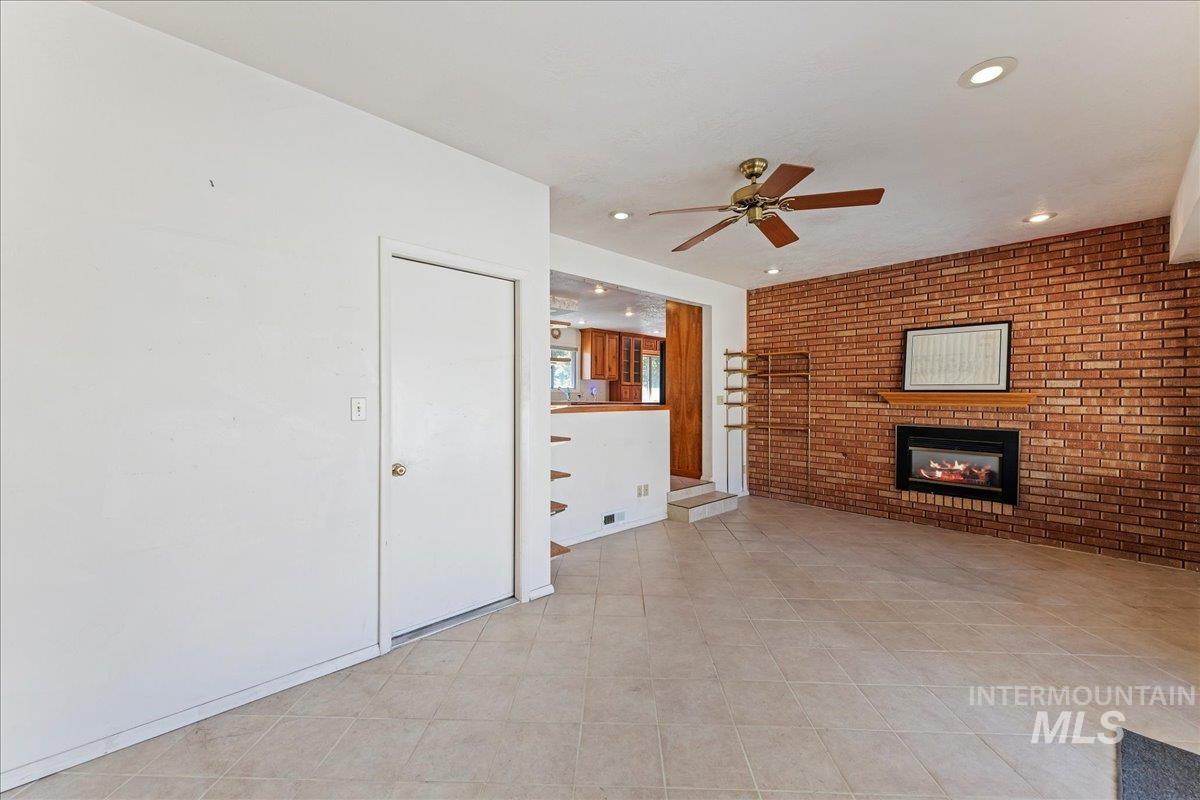 Unfurnished living room featuring brick wall, a fireplace, a ceiling fan, light tile patterned floors, and recessed lighting