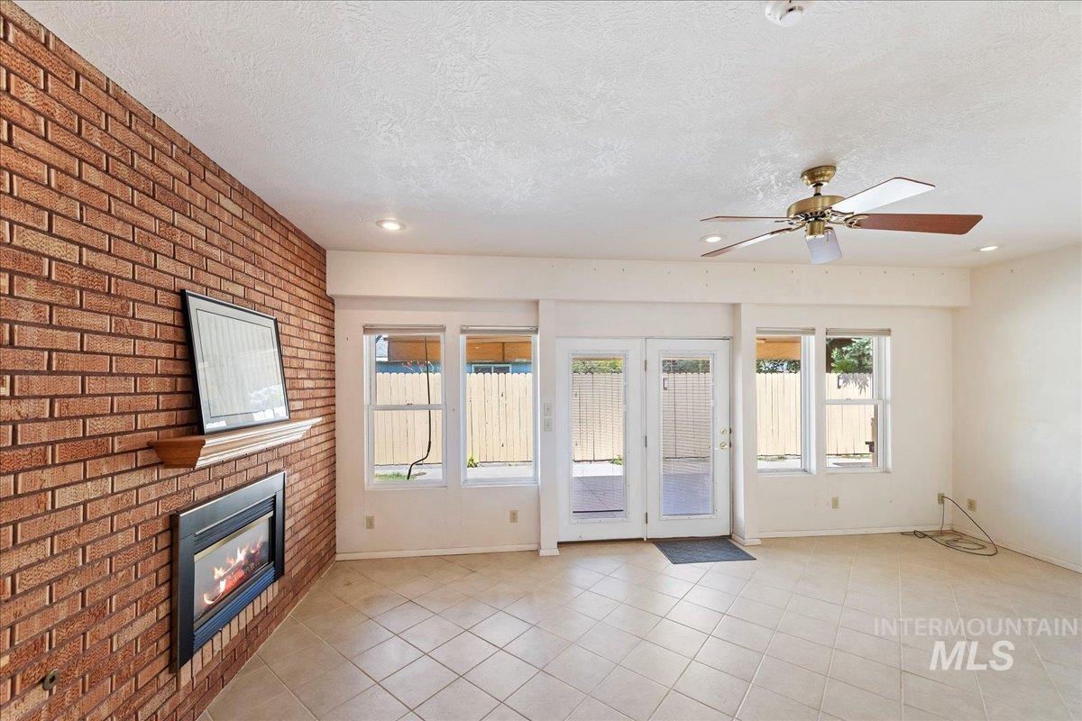 Unfurnished living room featuring light tile patterned floors, a textured ceiling, a brick fireplace, a ceiling fan, and recessed lighting
