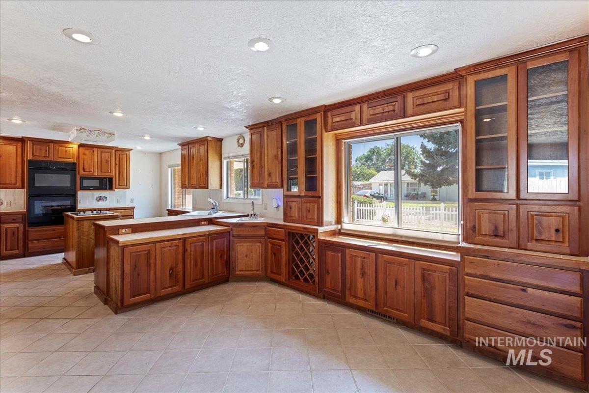 Kitchen featuring brown cabinets, a peninsula, glass insert cabinets, recessed lighting, and black appliances