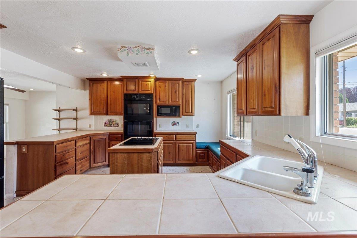 Kitchen featuring brown cabinets, a peninsula, healthy amount of natural light, black appliances, and recessed lighting