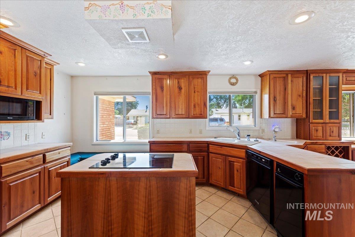 Kitchen featuring backsplash, brown cabinets, light tile patterned floors, recessed lighting, and black appliances