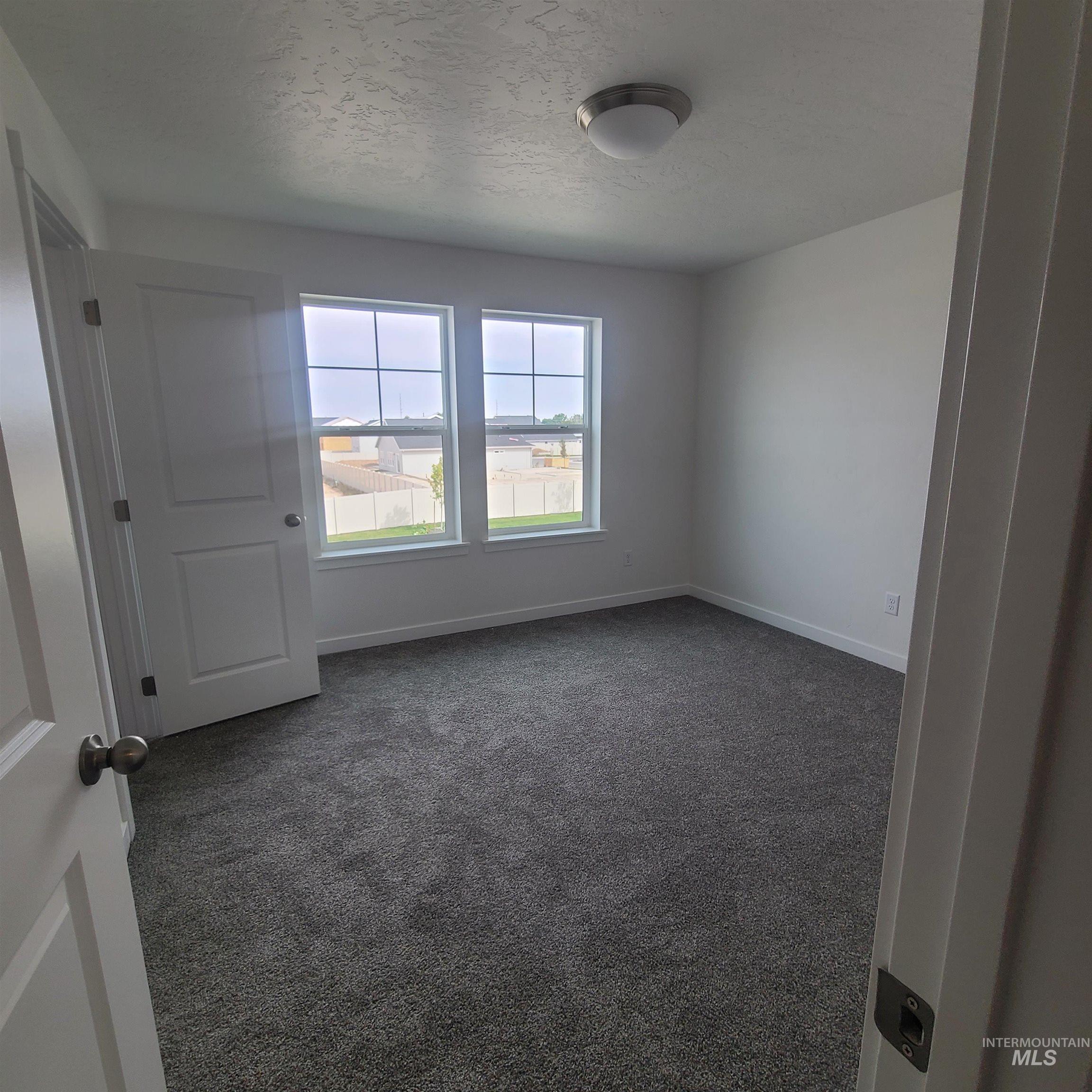 Carpeted spare room with a textured ceiling and baseboards