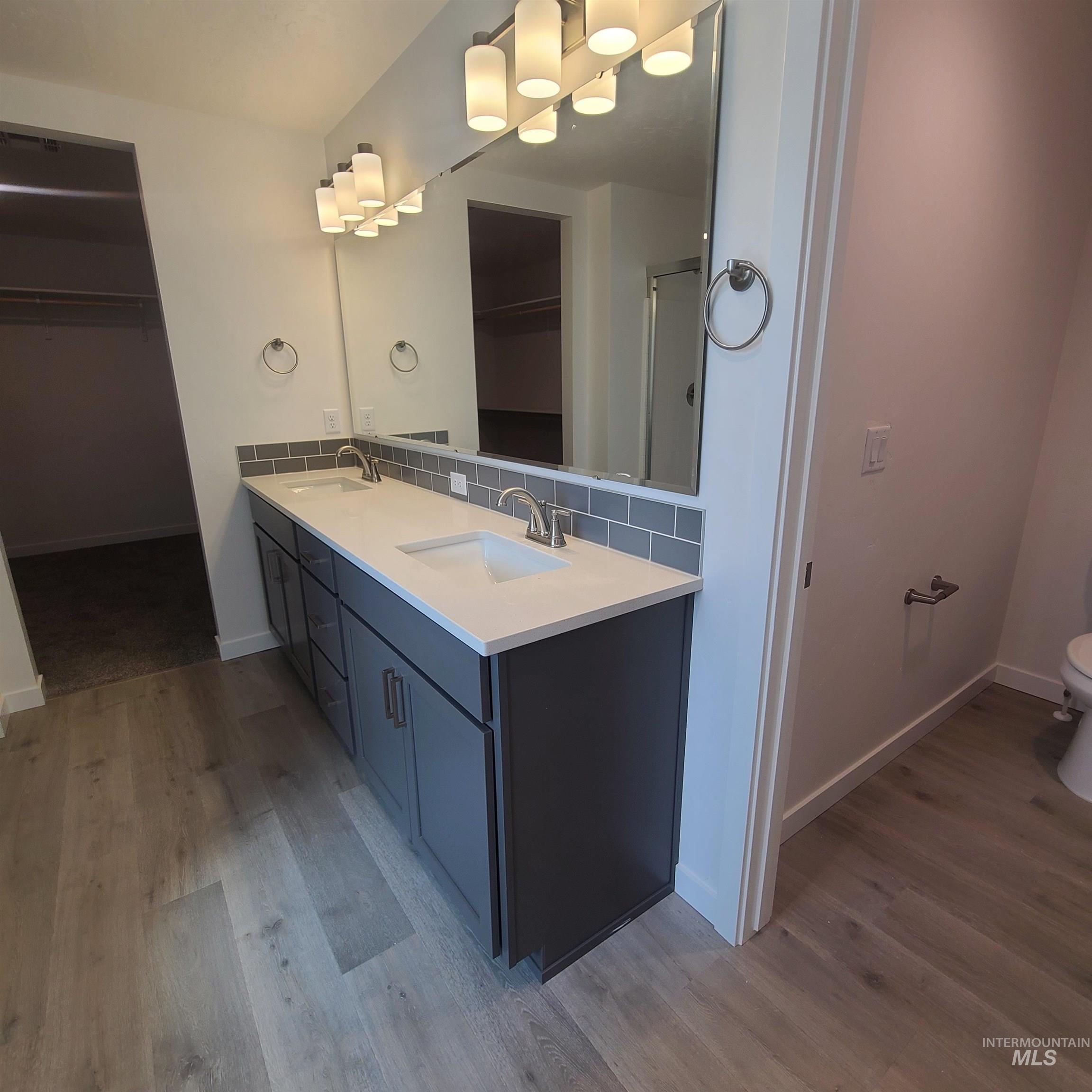 Full bath with decorative backsplash, a spacious closet, double vanity, and light wood finished floors