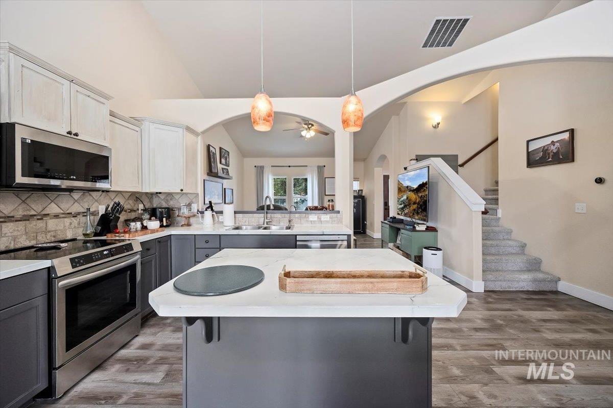 Kitchen with appliances with stainless steel finishes, pendant lighting, gray cabinets, tasteful backsplash, and a center island