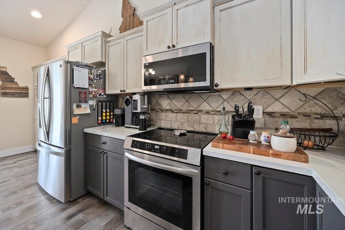 Kitchen featuring appliances with stainless steel finishes, gray cabinets, light wood-type flooring, tasteful backsplash, and recessed lighting