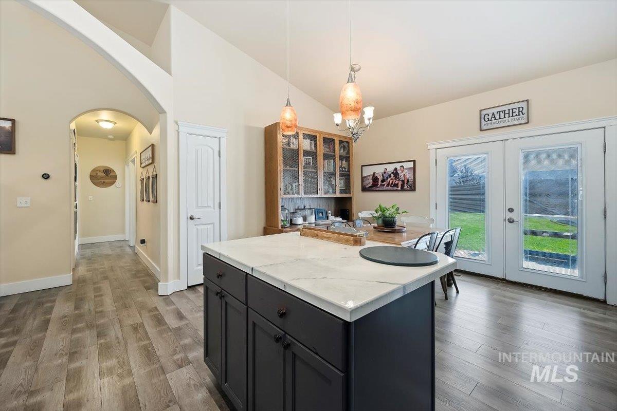 Kitchen with pendant lighting, arched walkways, a center island, light wood-type flooring, and high vaulted ceiling