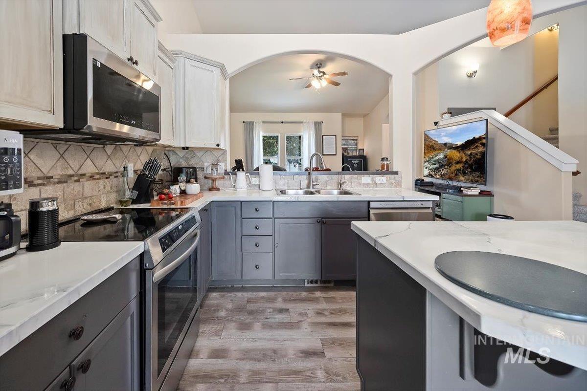 Kitchen featuring stainless steel appliances, gray cabinetry, backsplash, light wood finished floors, and ceiling fan