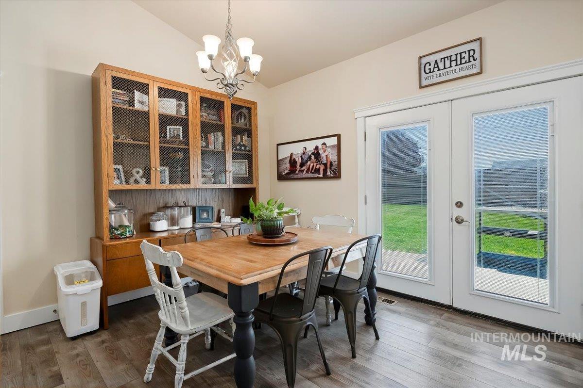 Dining room with french doors, dark wood finished floors, a chandelier, and lofted ceiling